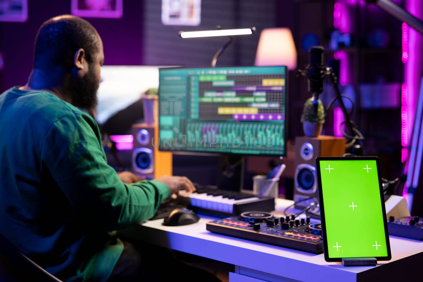 Composer editing his audio files and recordings on daw software, sitting next to a greenscreen display. Skilled sound technician uses mixing and mastering gear to produce new material.