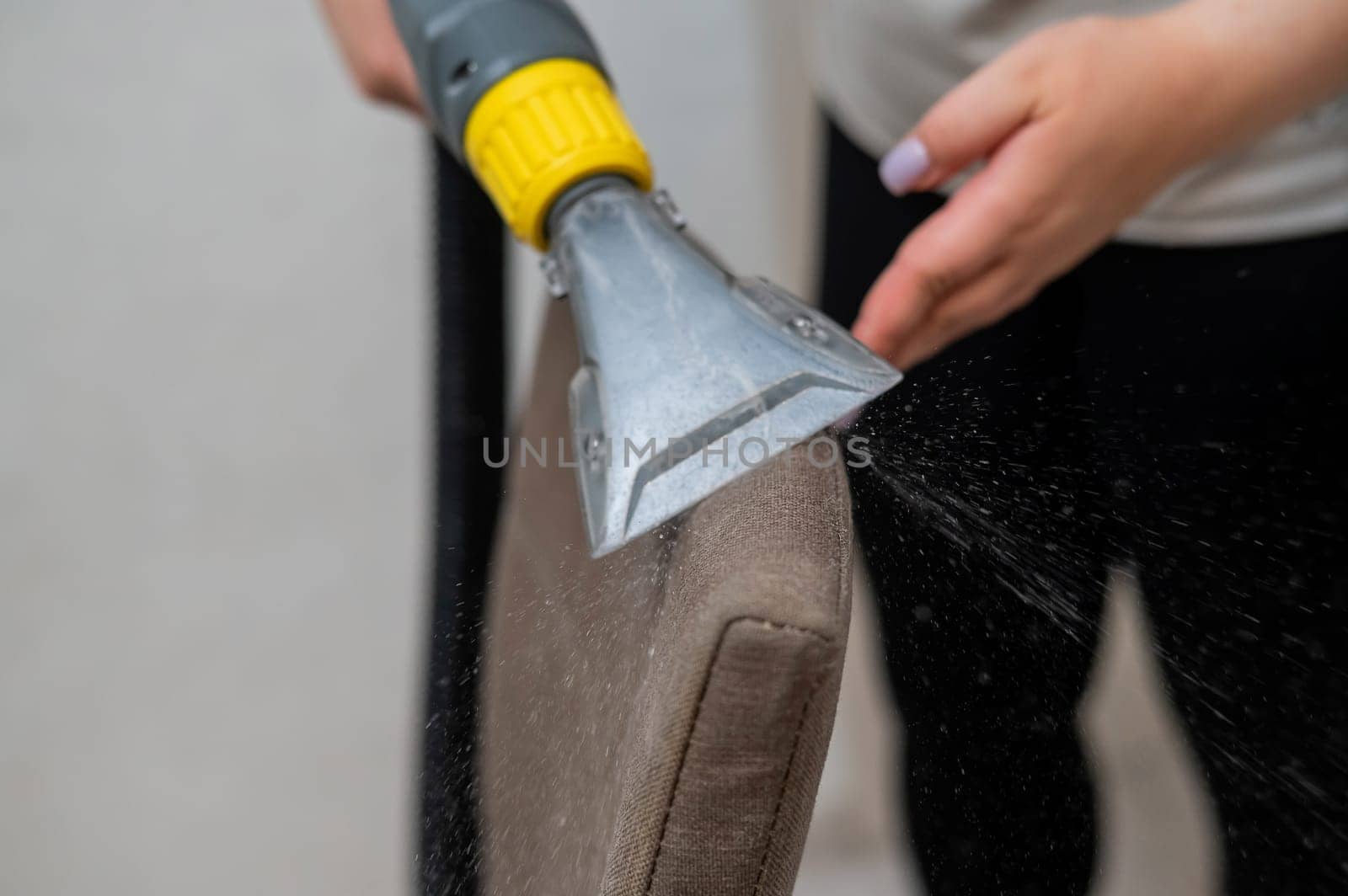 Woman cleaning the back of a fabric chair with a professional washing vacuum cleaner