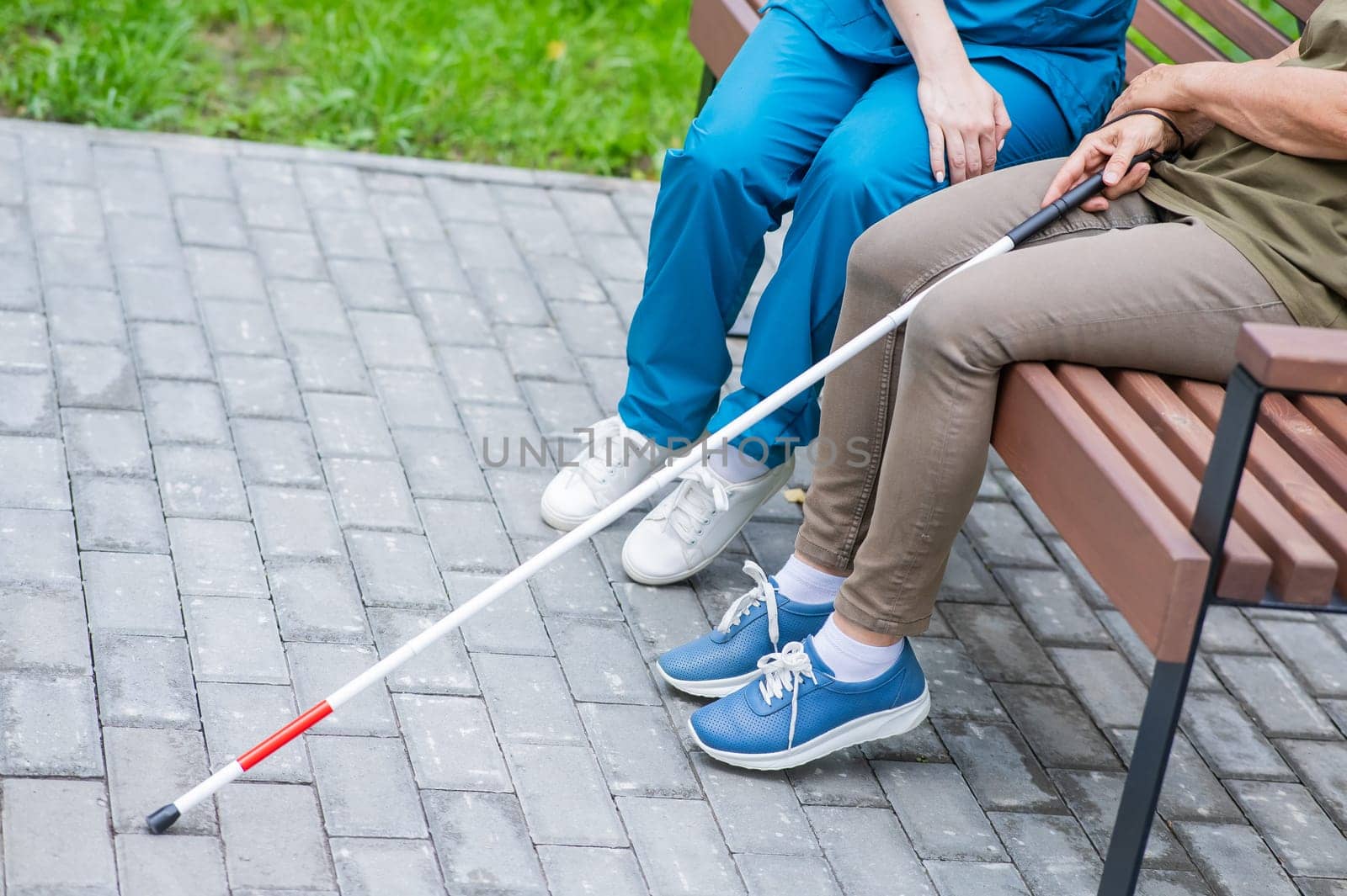 A nurse and an elderly blind woman are sitting on a bench in the park. Close up of legs