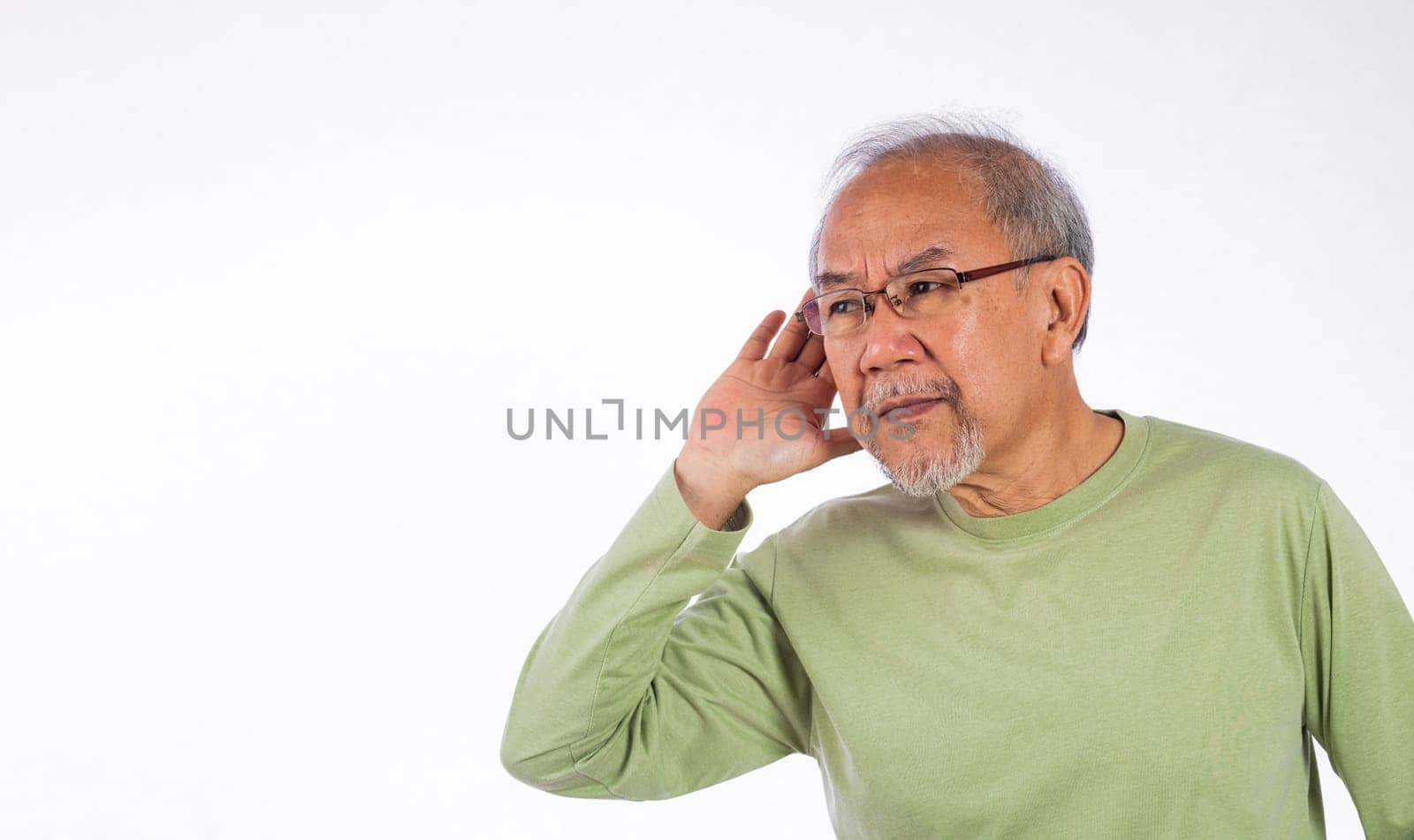 Portrait Asian old man with glasses and a beard listening to sound something, possibly engaged in conversation or trying to understand a message, hand on ear hearing a rumor isolated by Sorapop