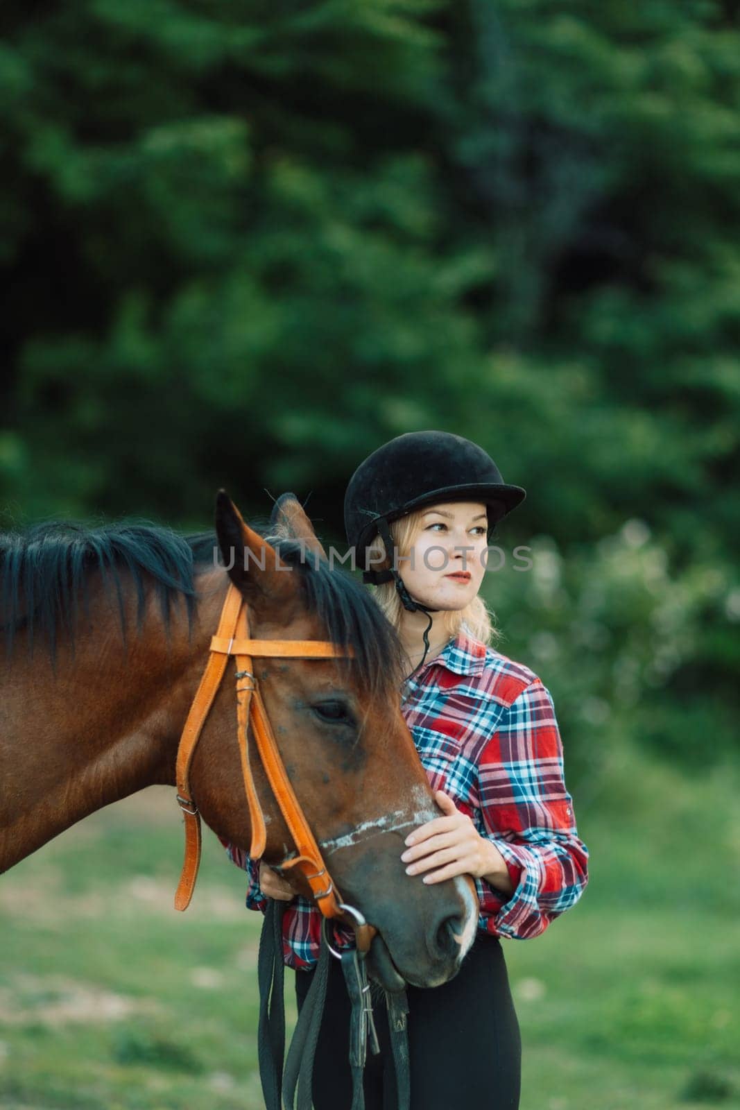 Happy blonde with horse in forest. Woman and a horse walking through the field during the day. Dressed in a plaid shirt and black leggings