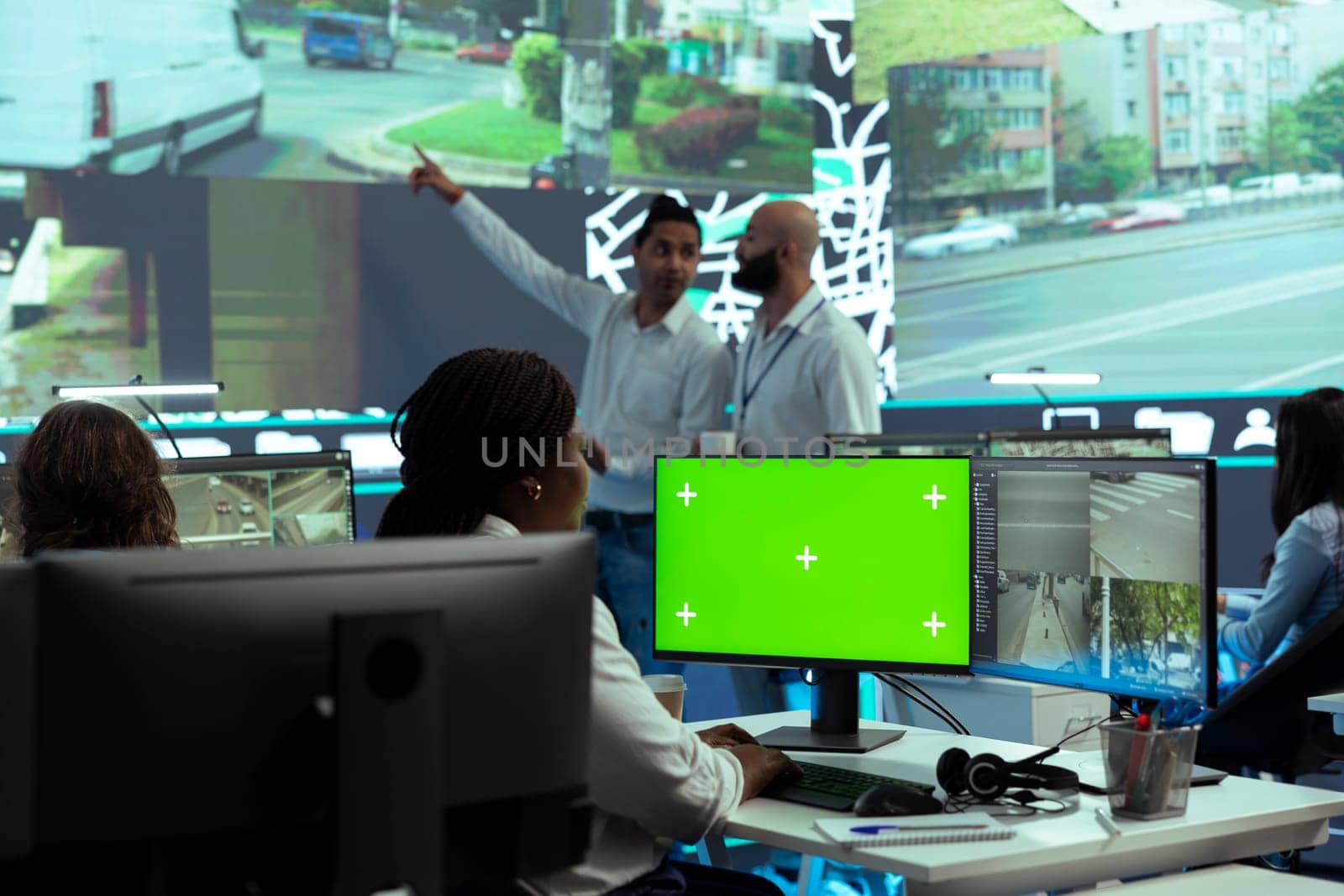 African american employee monitoring delivery trucks on CCTV cameras, using a greenscreen display in control center. Dispatch operator uses gps tracking satellite map, traffic radar.