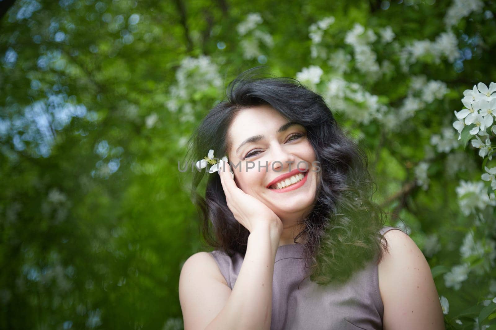 Joyous brunette woman near Blossoms of apple tree in a Spring Garden outdoors. The Concept of face and body care. The scent of perfume and tenderness