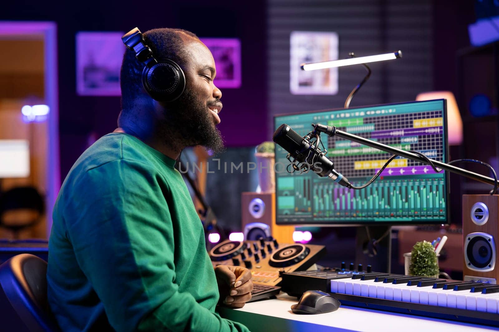 Male sound engineer singing a new song to record audio on microphone, editing music with mixing console and gear in home studio. Artist adjusting volume levels with stereo tools.