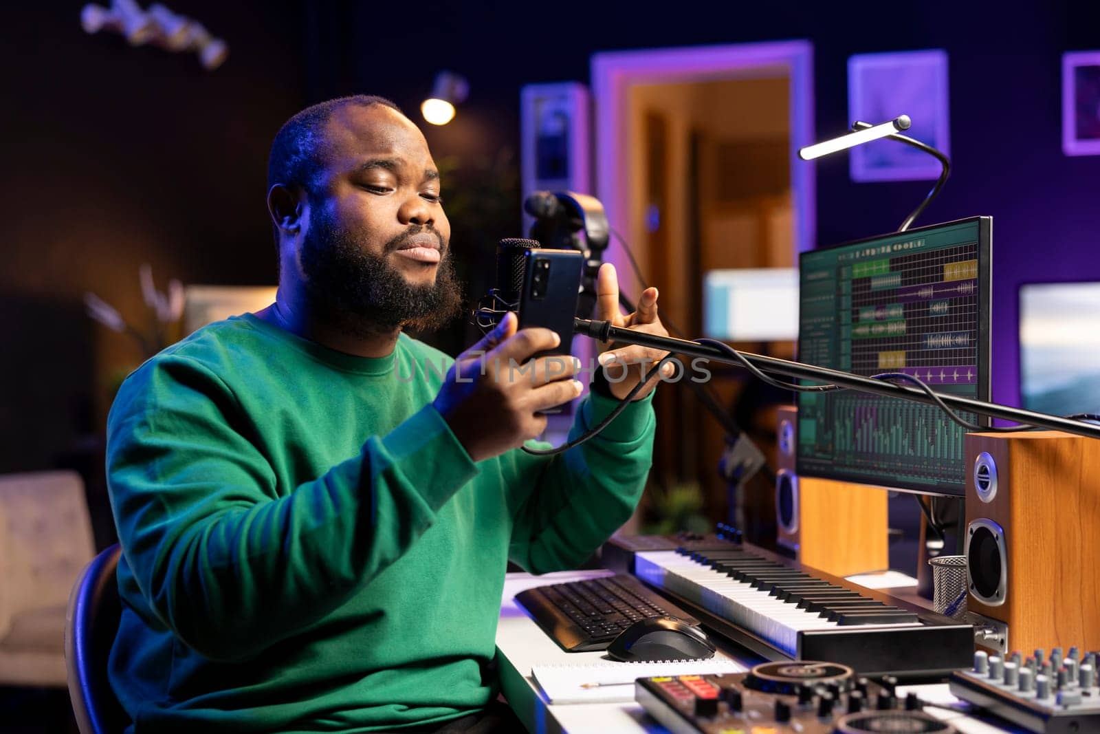 African american songwriter singing his new creation in home studio, recording audio files of his new song for the acoustic version. Young artist musician uses phone to read notes and verses.