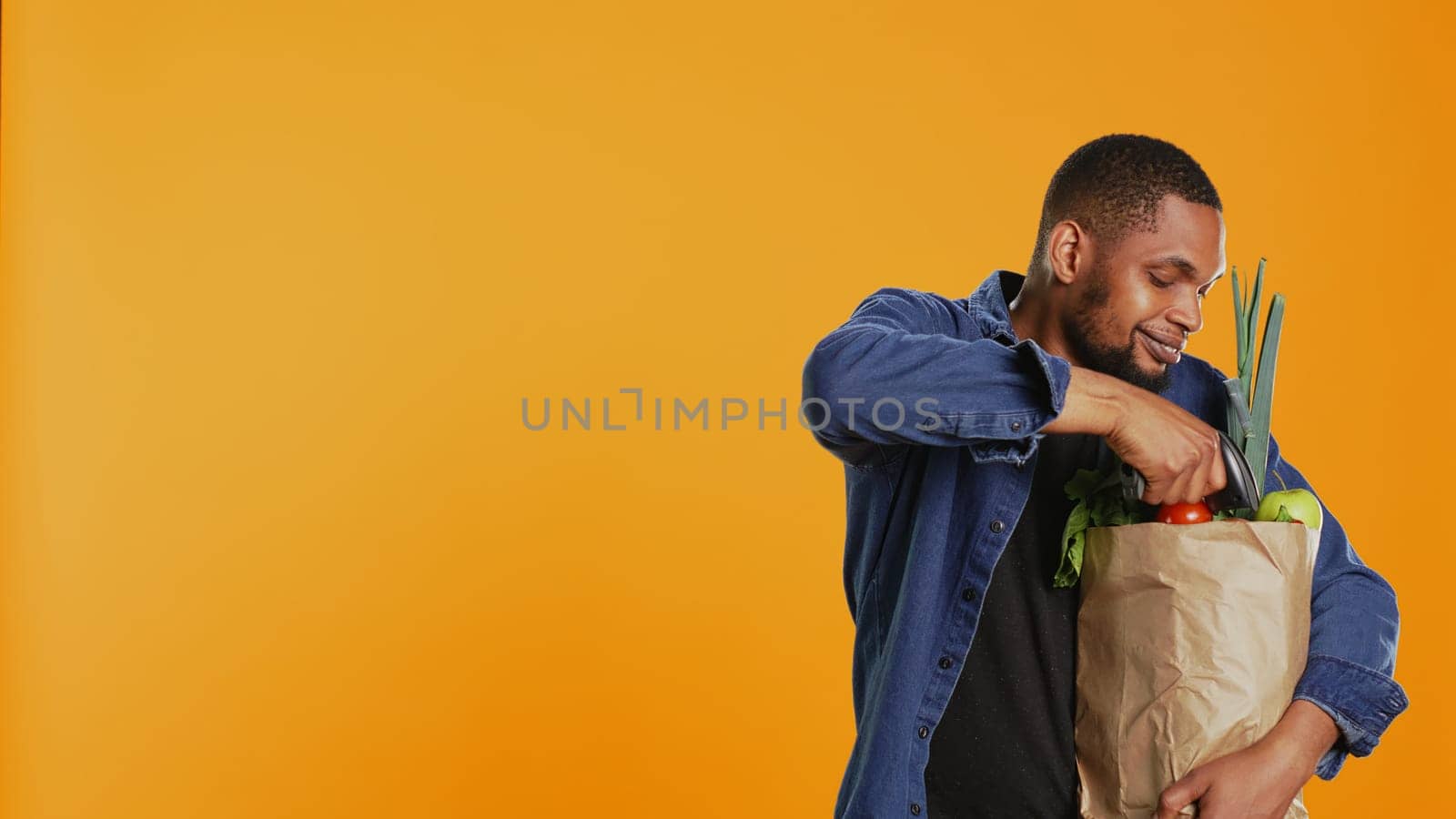 African american young man scanning all eco friendly produce in studio, buying organic natural fruits and vegetables. Male model using a scanner to check fresh groceries. Camera B.