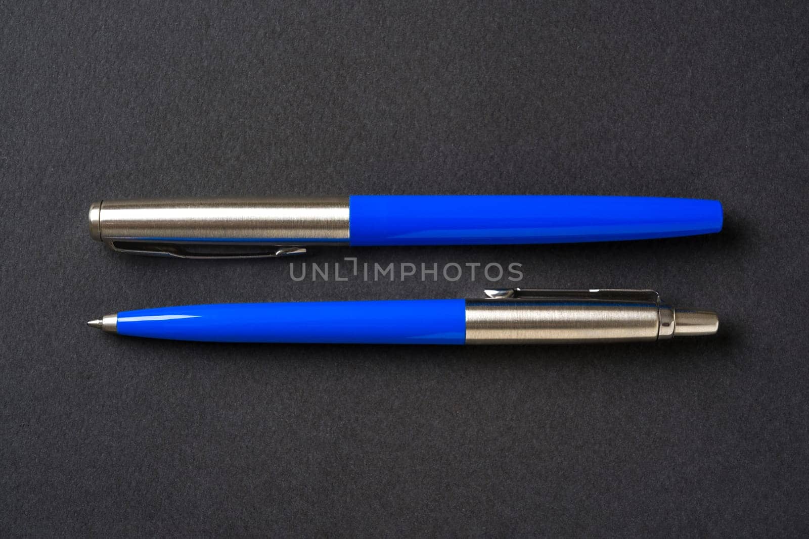 Blue plastic and metal ballpoint pen and fountain pen on dark gray isolated background