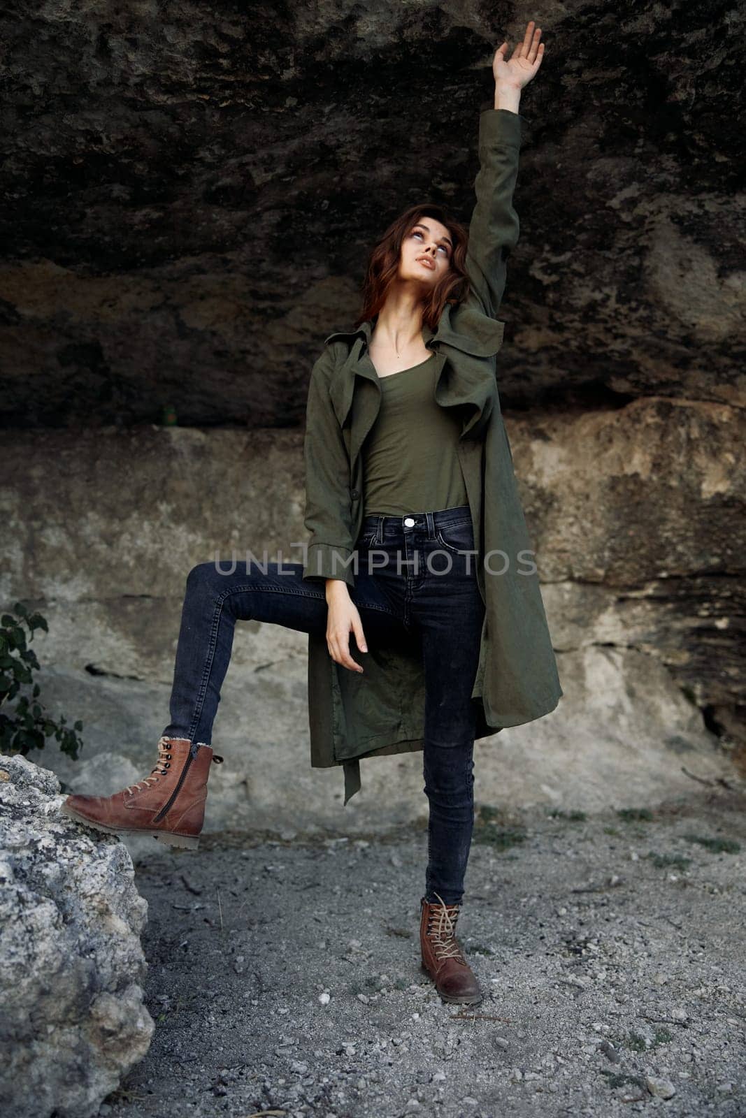 Woman in green coat standing triumphantly on rock with arms raised high