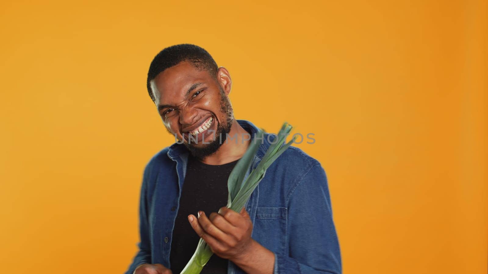 Happy person having fun playing guitar at a leek in studio, acting funny and mimicking a green onion as a musical instrument. Young guy being silly with organic vegetables. Camera A.