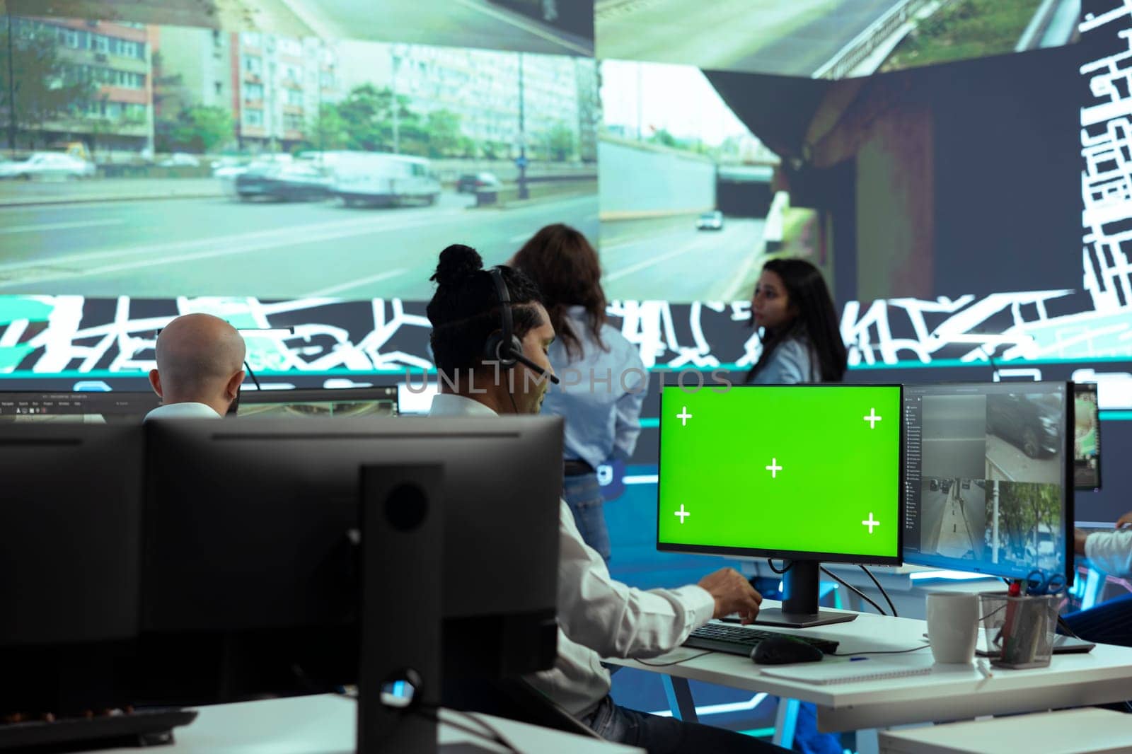 Indian employee operates on mockup display next to CCTV real time video, monitoring couriers activity through urban traffic via public surveillance system. Dispatcher in control center.