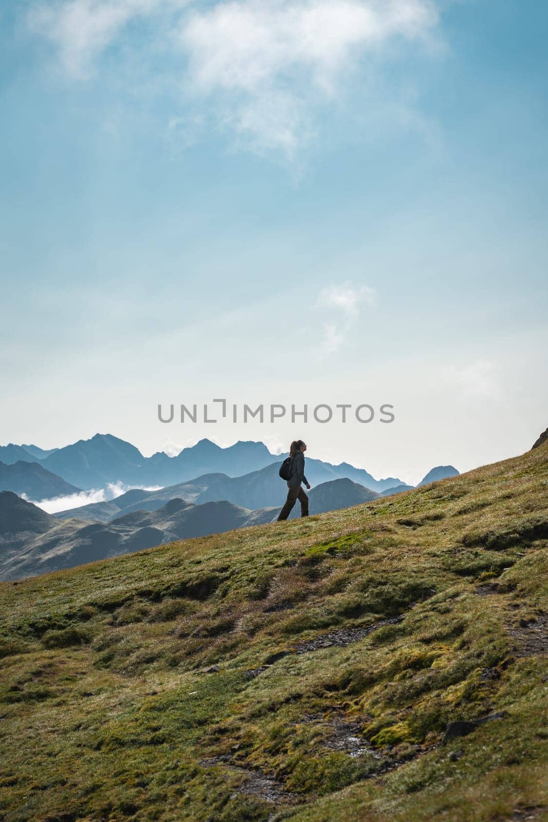 A person is leisurely strolling up a grassy slope in the scenic mountains by PaulCarr