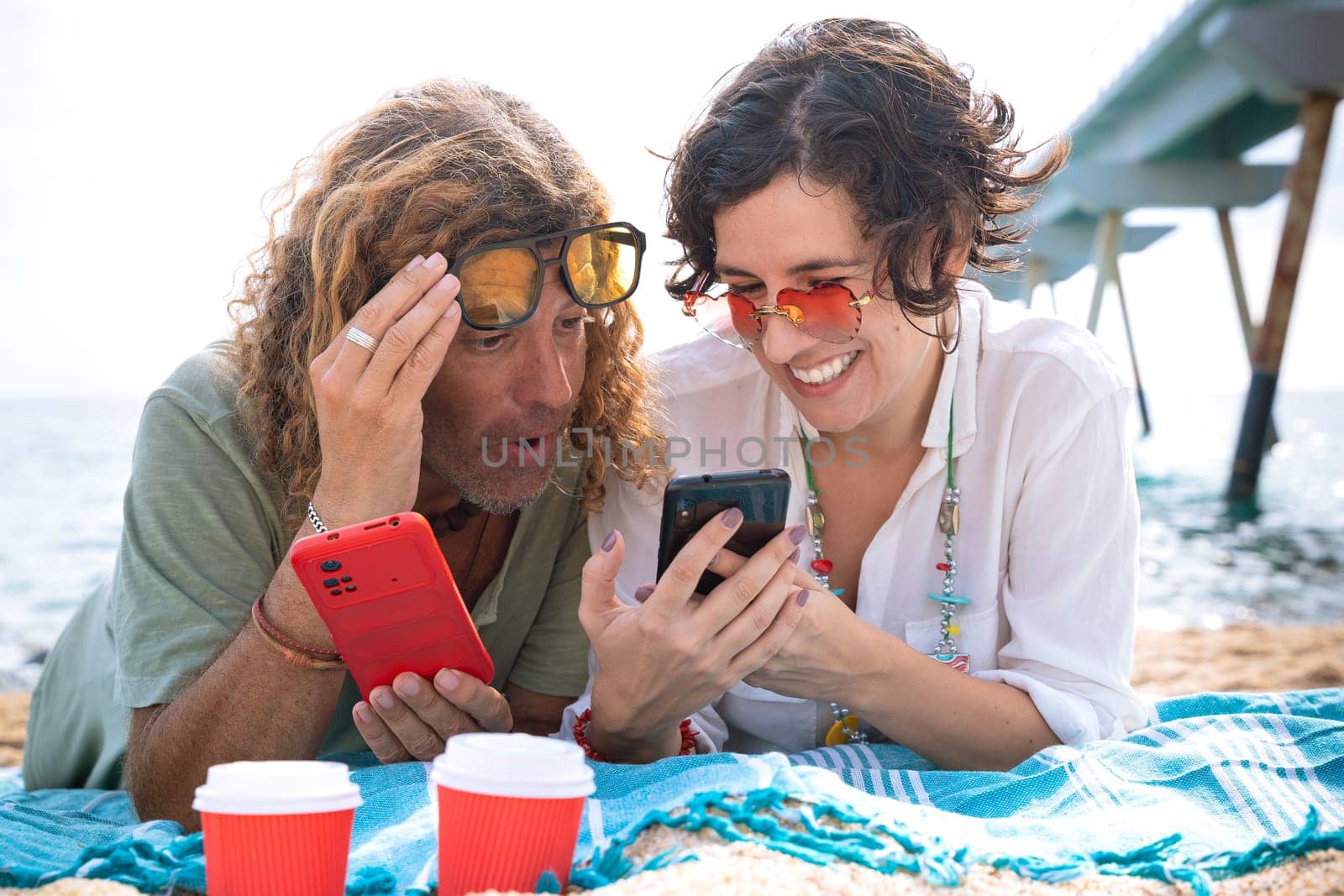 Smiling couple on the beach browsing smartphone apps. by mariaphoto3