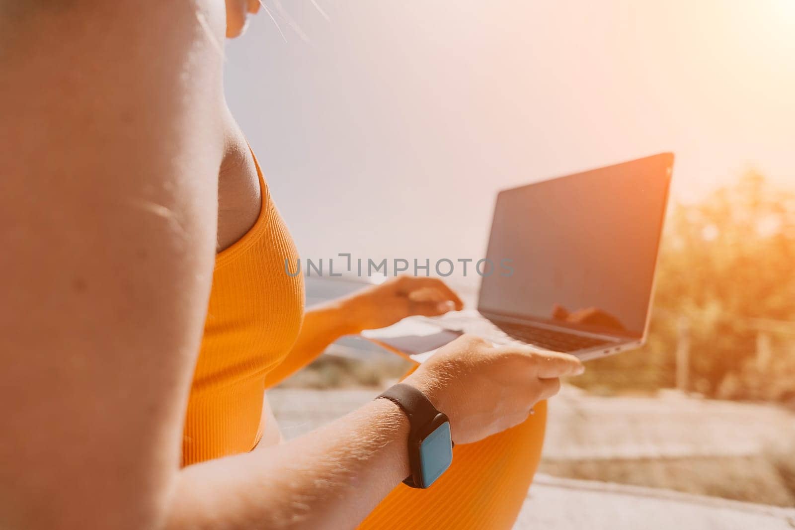 Digital nomad, Business woman working on laptop by the sea. Pretty lady typing on computer by the sea at sunset, makes a business transaction online from a distance. Freelance, remote work on vacation