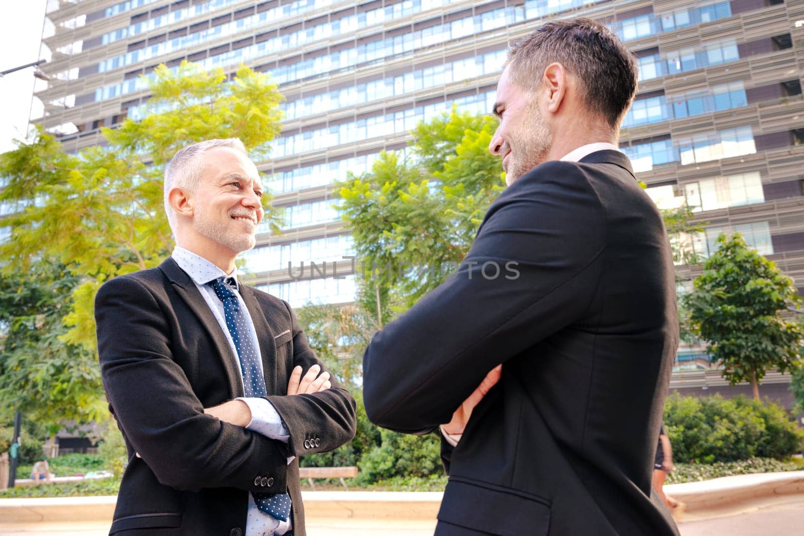 Two smiling businessmen standing in front of each other with arms crossed by mariaphoto3