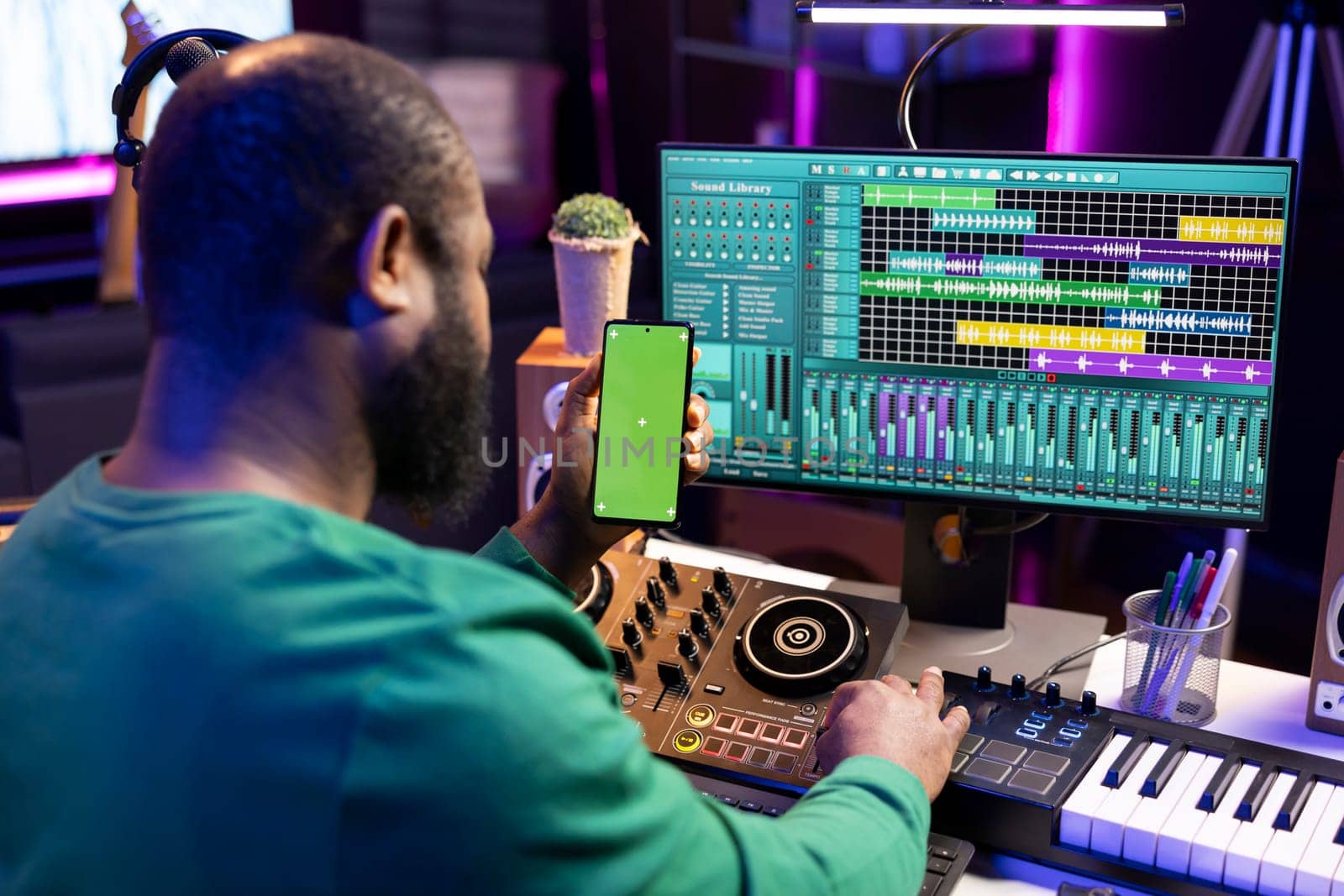 Male technician using mixing console and piano to edit tunes, having isolated mockup screen. Composer producing new music with mixing and mastering techniques in his home studio.