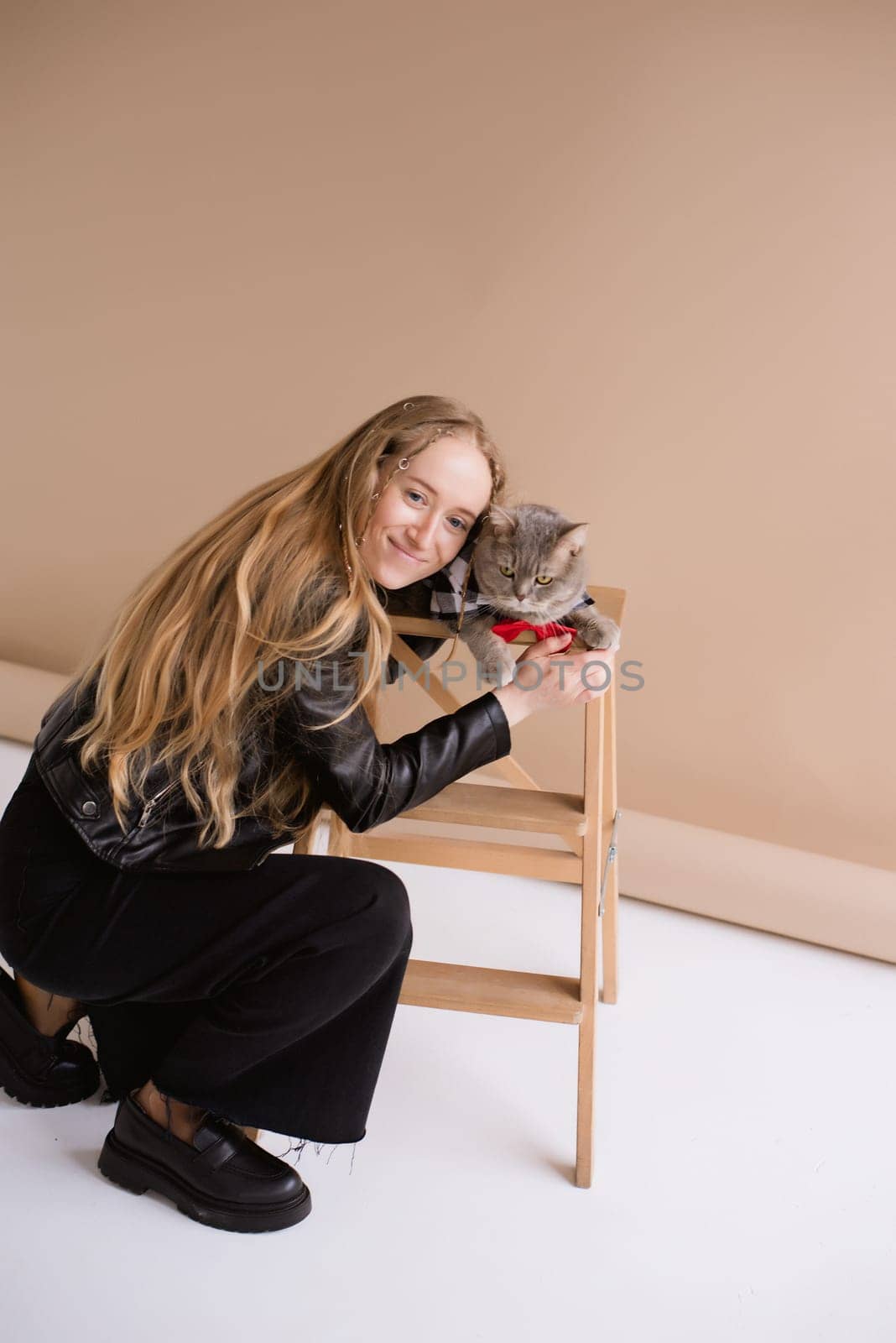 A woman natural blonde long hair smiling in a black clothes stand, sitting on photo studio. girl with pet scottish straight cat. portrait , vertical, close up