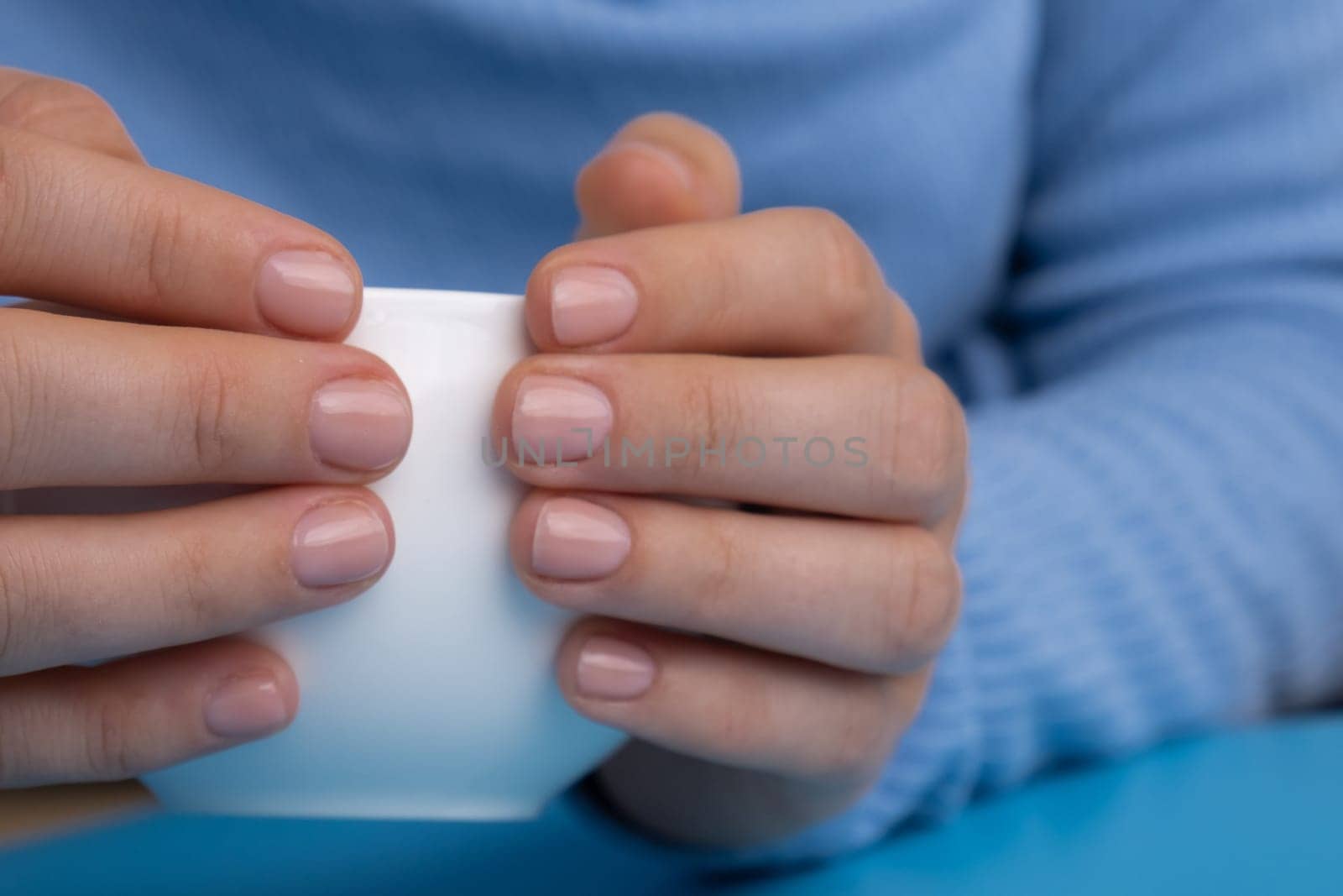 Pastel softness manicured nails on white cup on blue background. Woman showing her new manicure in colors of pastel palette. Simplicity decor fresh spring vibes earth-colored neutral tones design