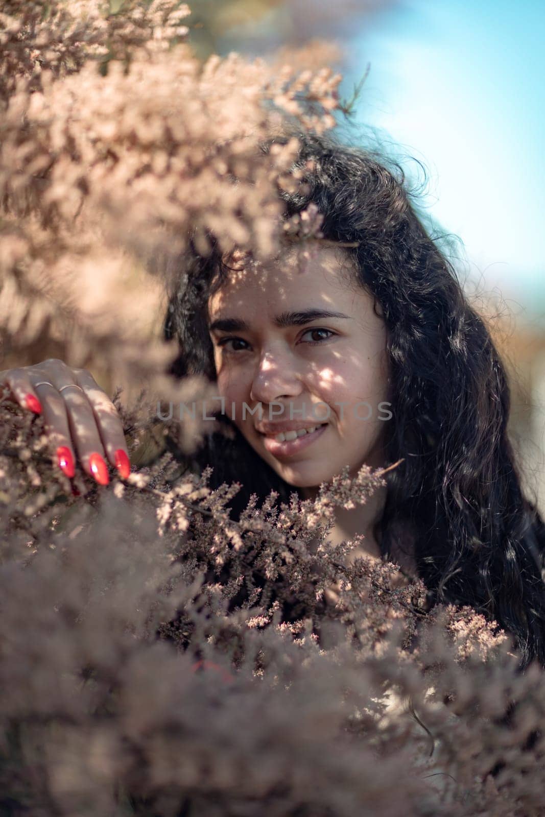 A woman is standing in a field of brown leaves. She is looking at the camera with a serious expression