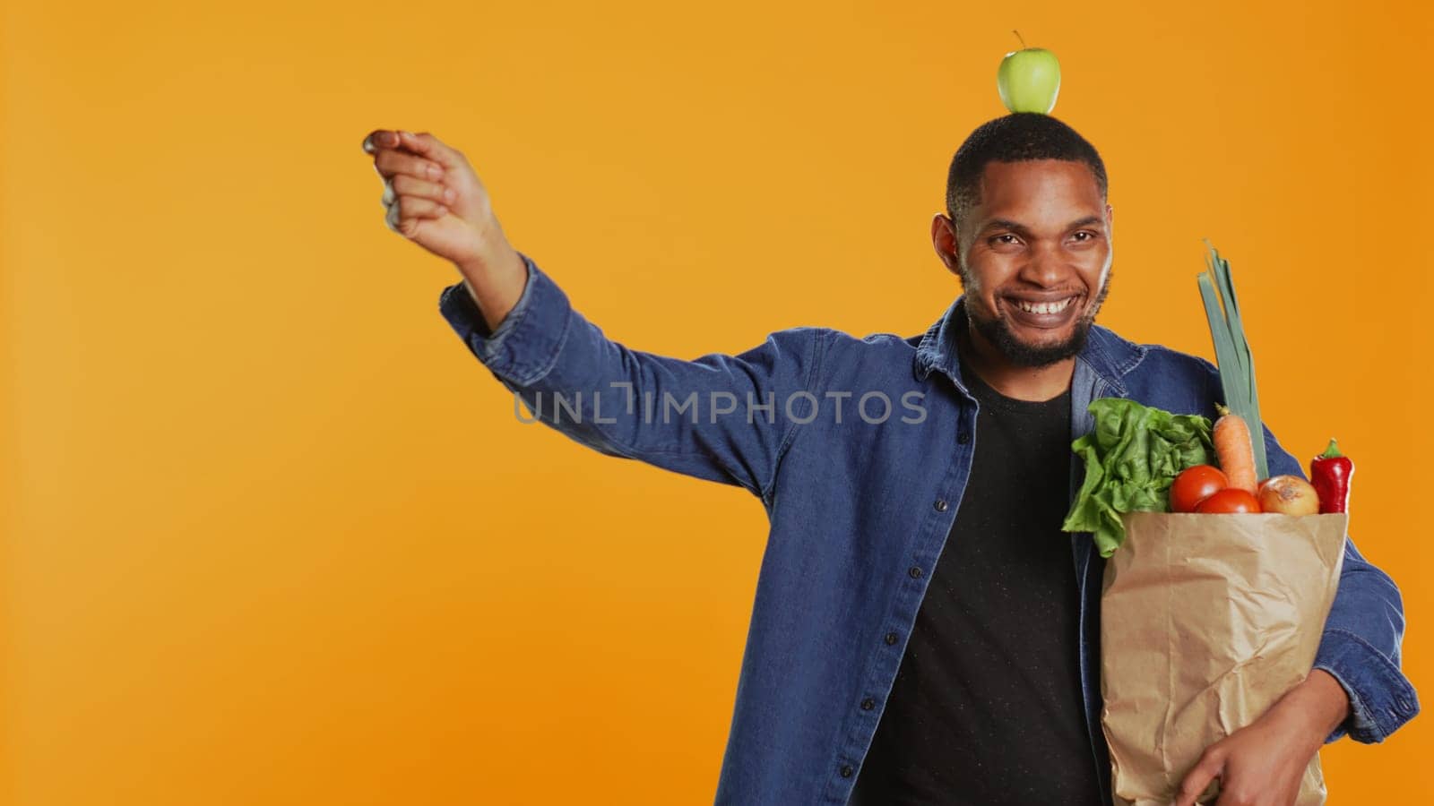 Playful vegan guy dancing with an apple placed on his head, having fun trying to be balanced and not drop it. Confident happy man recommending homegrown local fresh produce. Camera B.