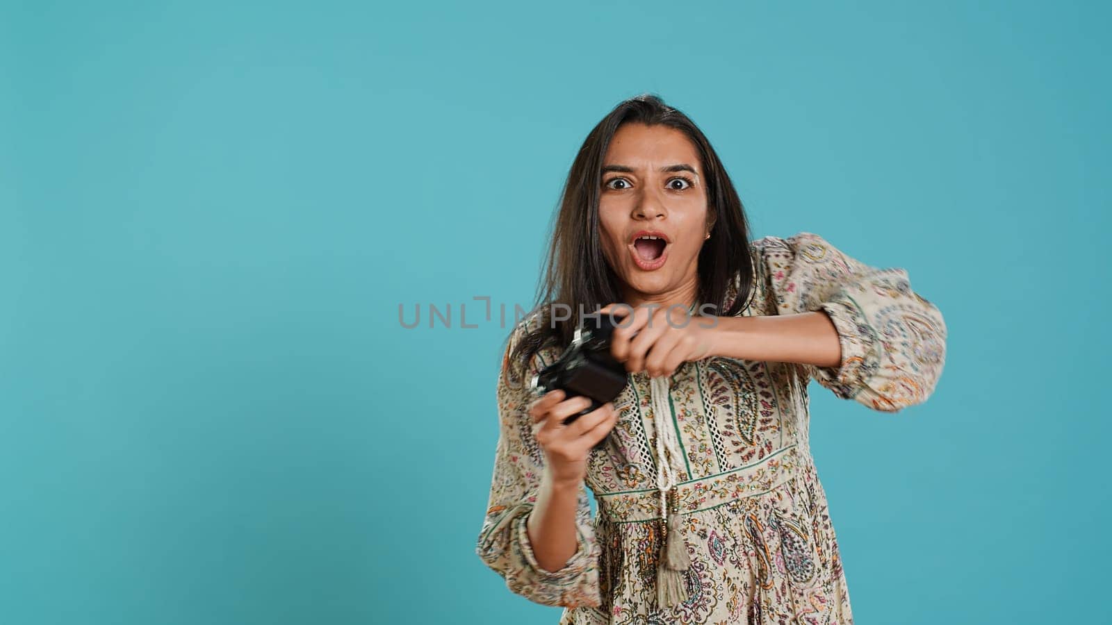 Competitive woman playing videogames with motion controlled controller, studio background. Indian Person participating in internet multiplayer racing game using gyroscope function on gamepad, camera A