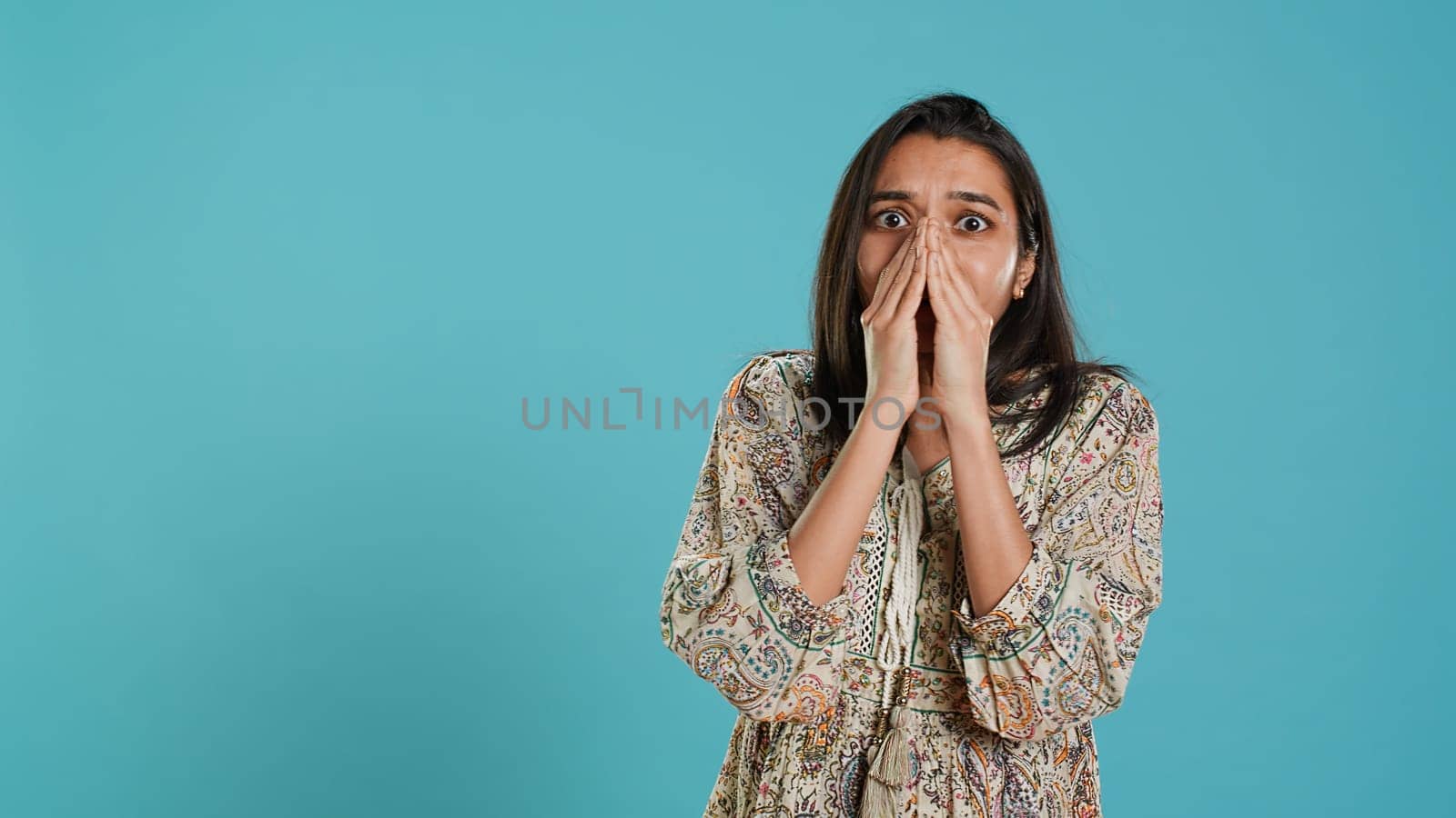 Anxious indian woman covering face with palms, worried about future, isolated over studio background. Tense person shocked by troubling news, gasping, feeling distressed, camera A