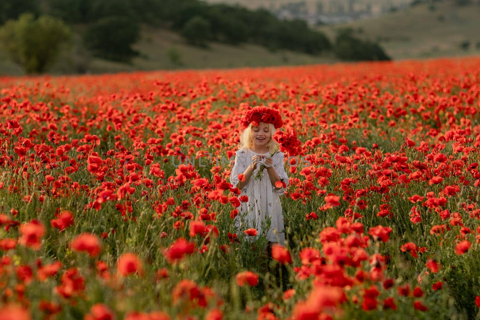 A young girl stands in a field of red poppies. The field is full of flowers and the girl is wearing a red headband