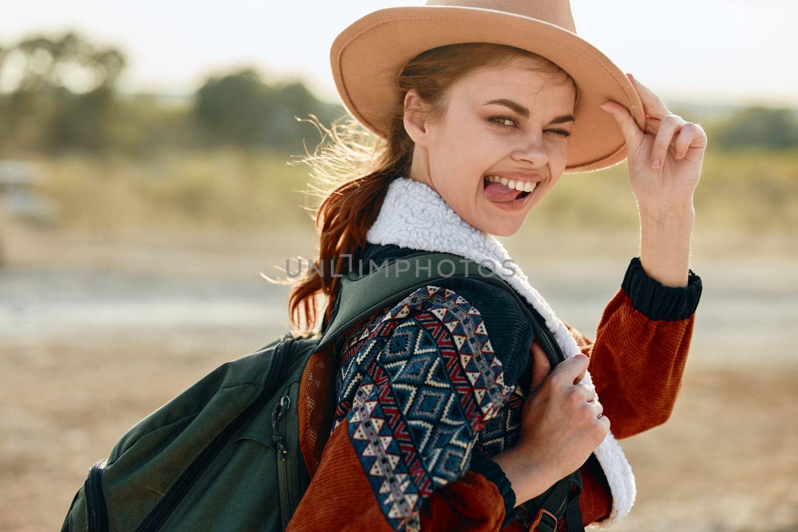 Happy woman in hat and sweater holding backpack in desert landscape