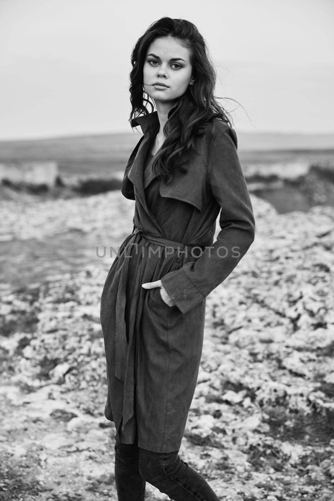 Mysterious woman in trench coat standing confidently on rocky hilltop
