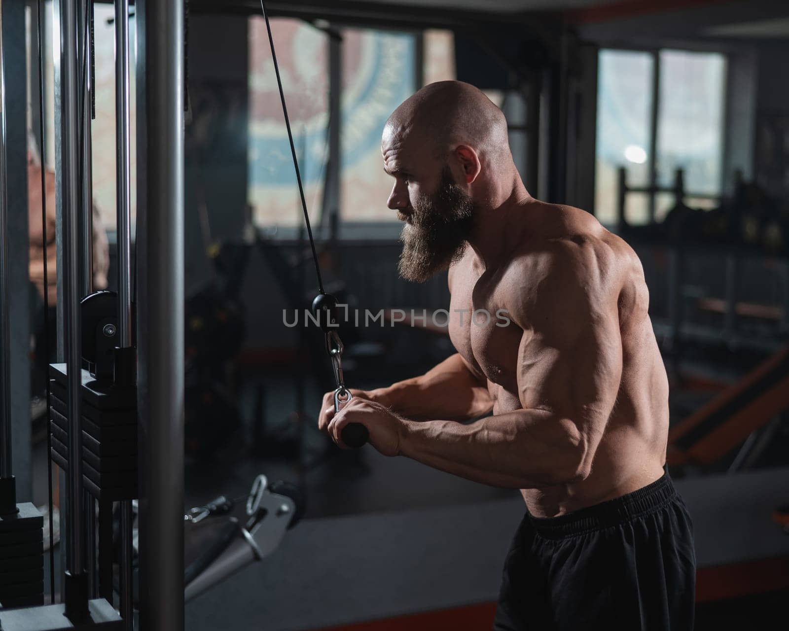 Bald Caucasian Bodybuilder doing heavy triceps exercises with cable