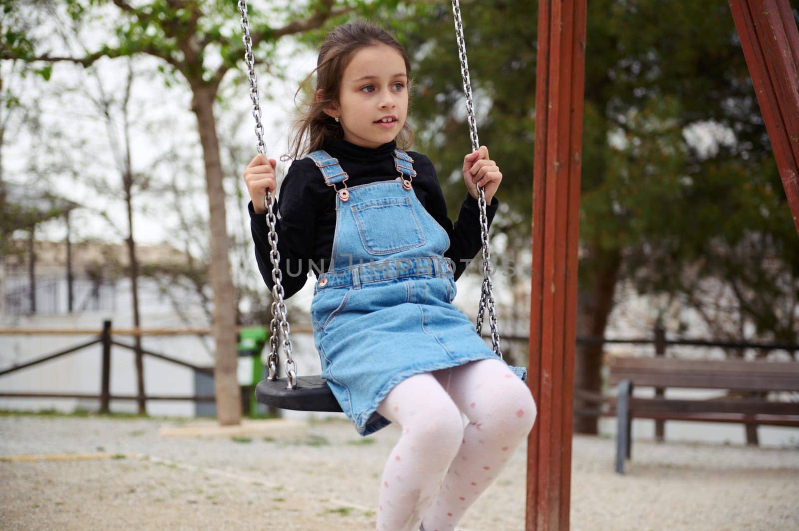 European cute child girl swinging on the outdoors playground. People. Happy carefree childhood concept. Lifestyle