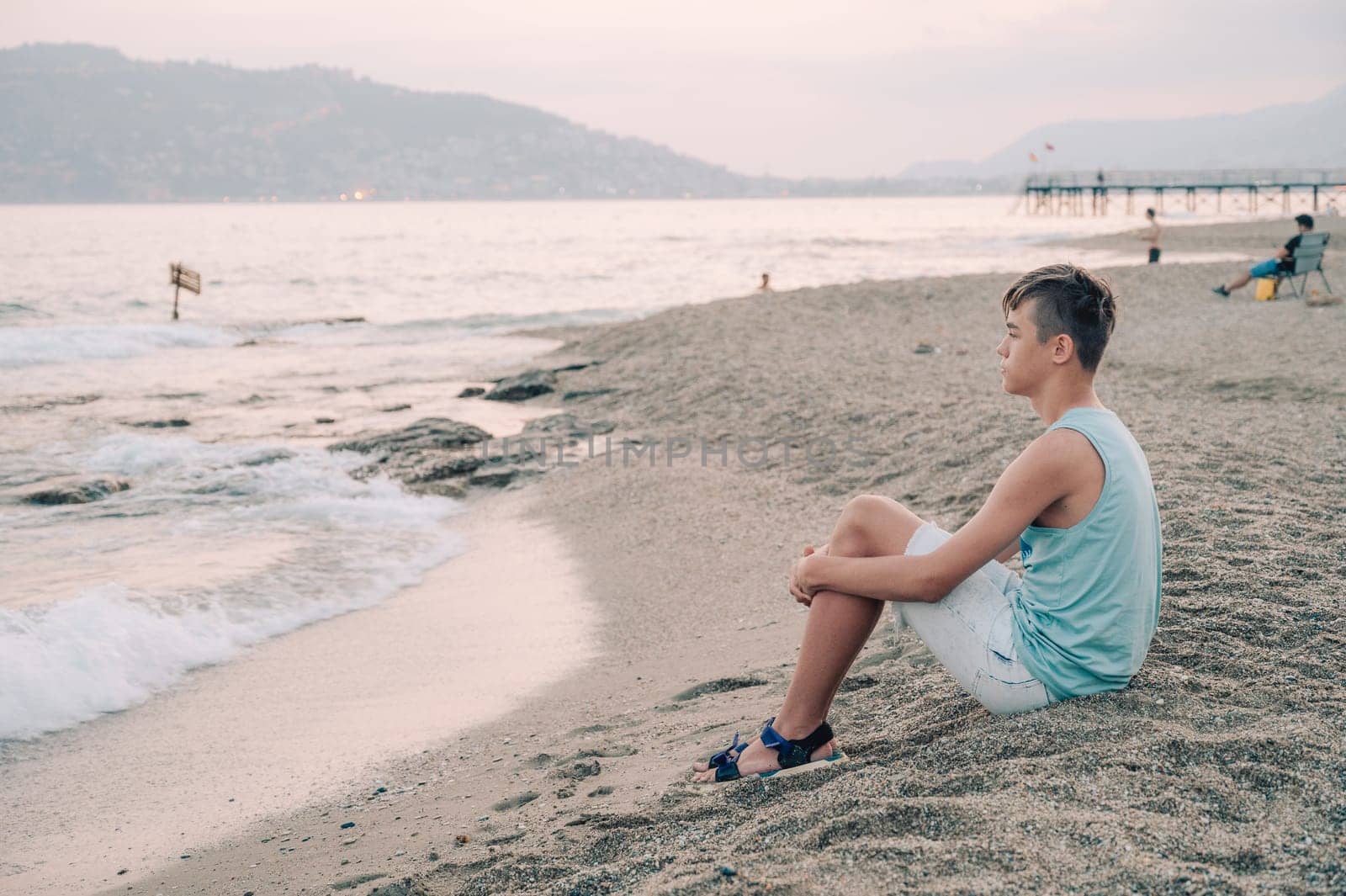 Boy teen sits on the beach and looks at the sea in Alanya city, Turkey. Travelling or vacation concept