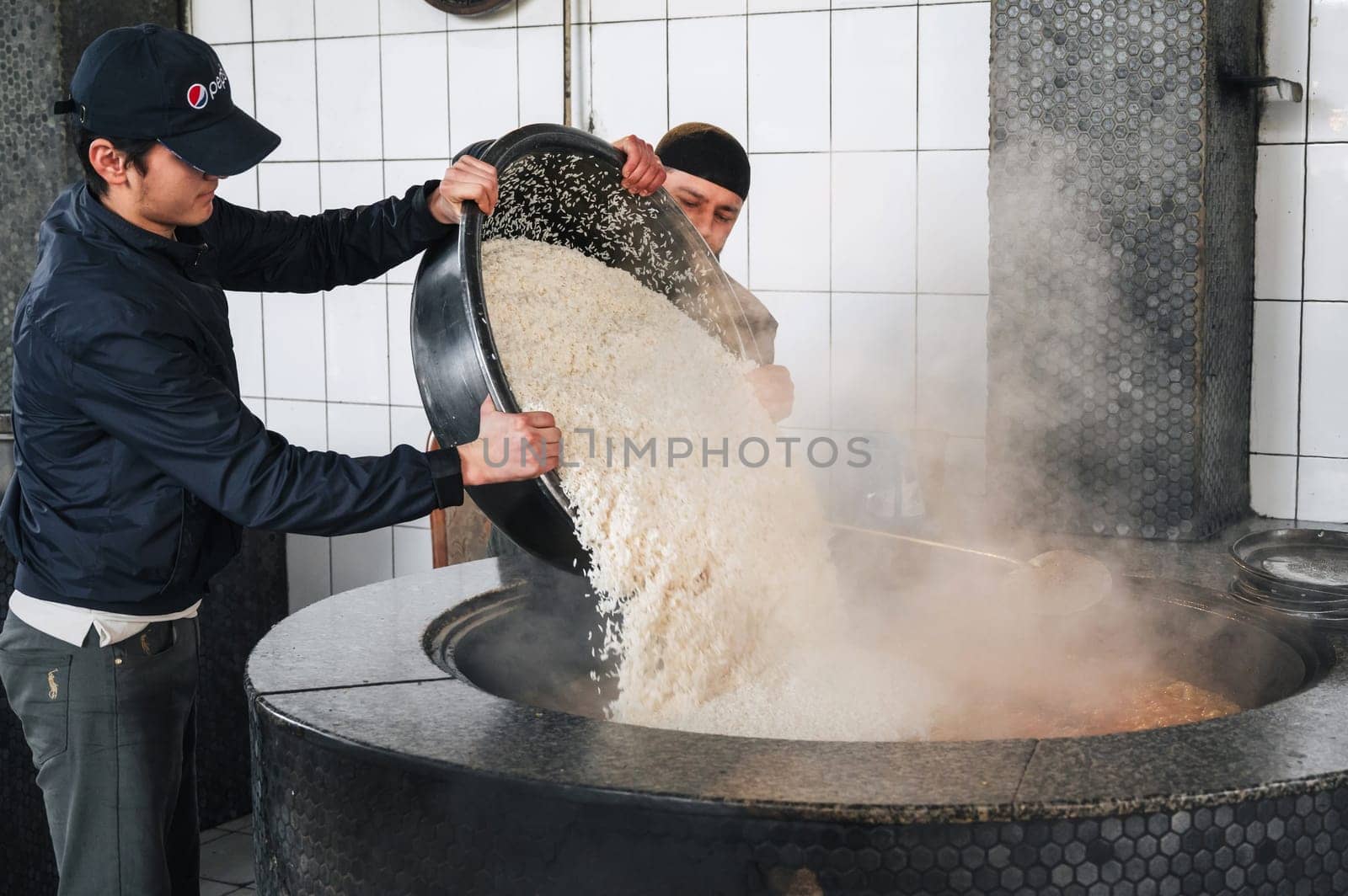 male chefs pour rice for traditional Uzbek pilaf into cauldron in kitchen in Central Asian Pilaf Center Besh Qozon. Tashkent, Uzbekistan - April 16, 2024 by alexkoral