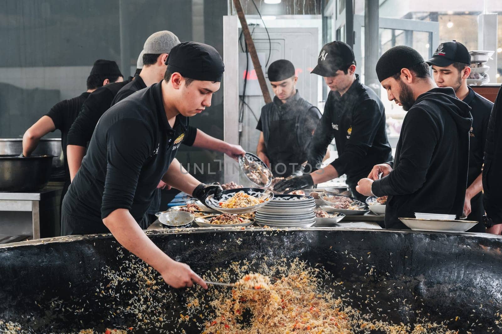 male cooks put ready-made traditional Uzbek pilaf from a big cauldron on plates in Central Asian Pilaf Center Besh Qozon. Tashkent, Uzbekistan - April 16, 2024