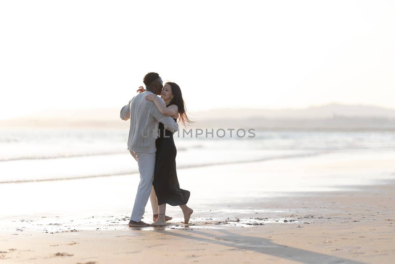 A couple is dancing on the beach, with the man holding the woman in his arms. The scene is romantic and intimate, with the couple enjoying each other's company in a beautiful natural setting