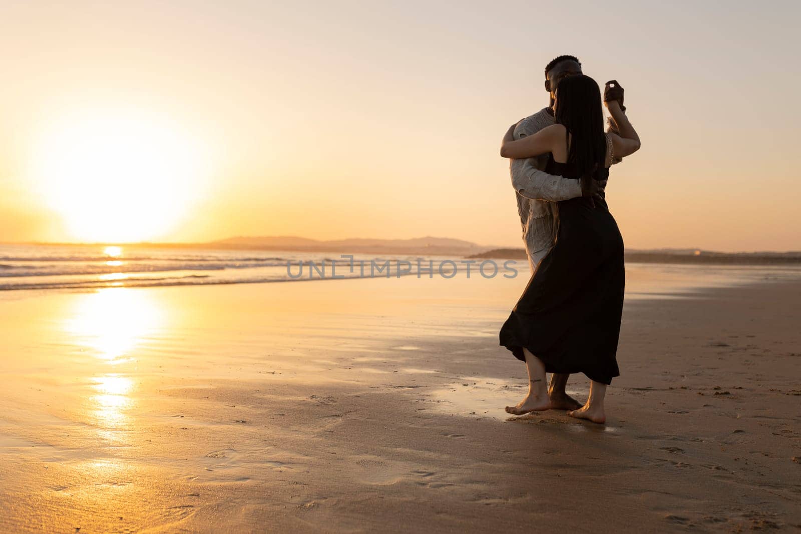 A couple dancing on the beach at sunset. The man is holding the woman's arm. Scene is romantic and peaceful