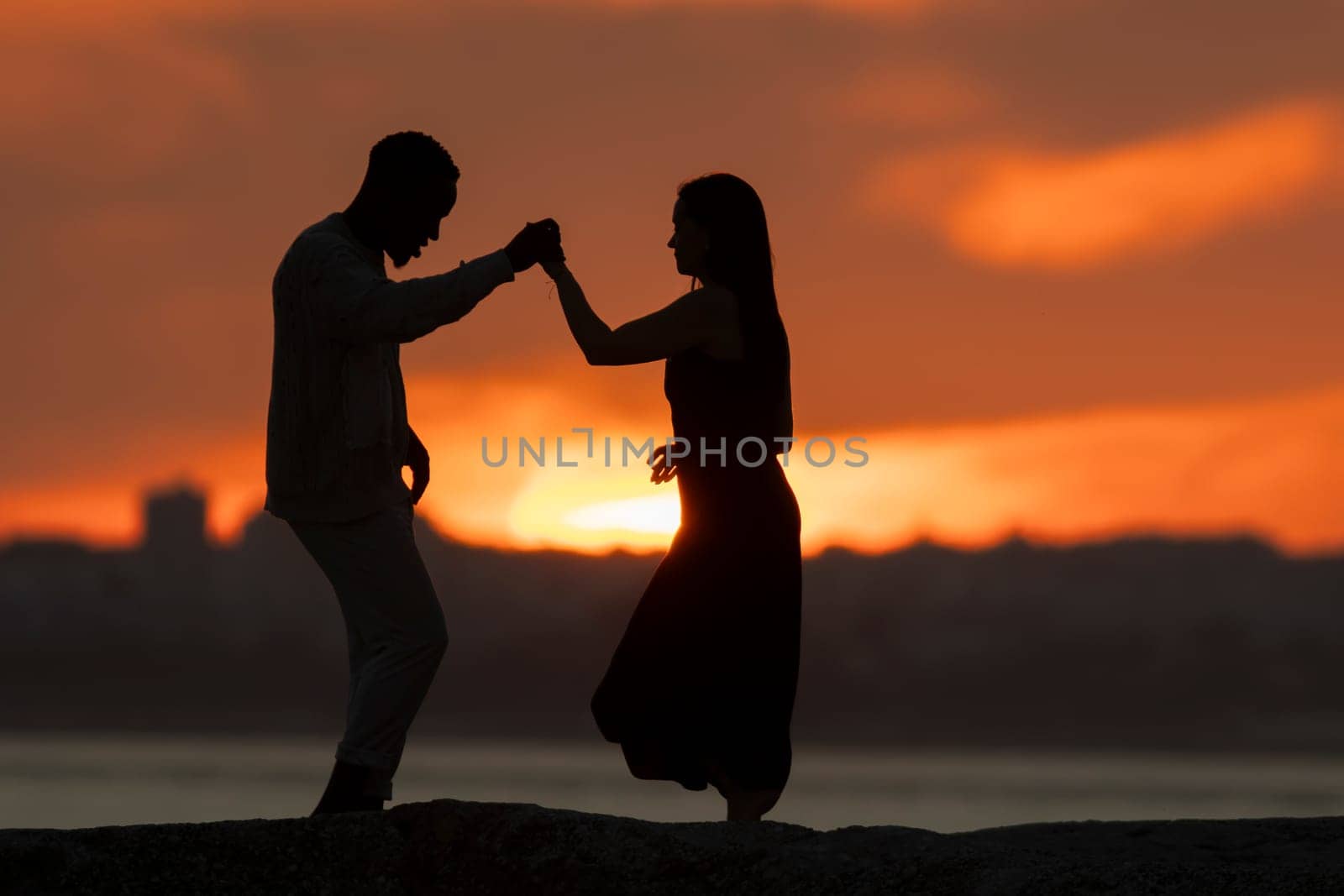 A couple dancing in the sunset. The man is wearing a white shirt and the woman is wearing a black dress