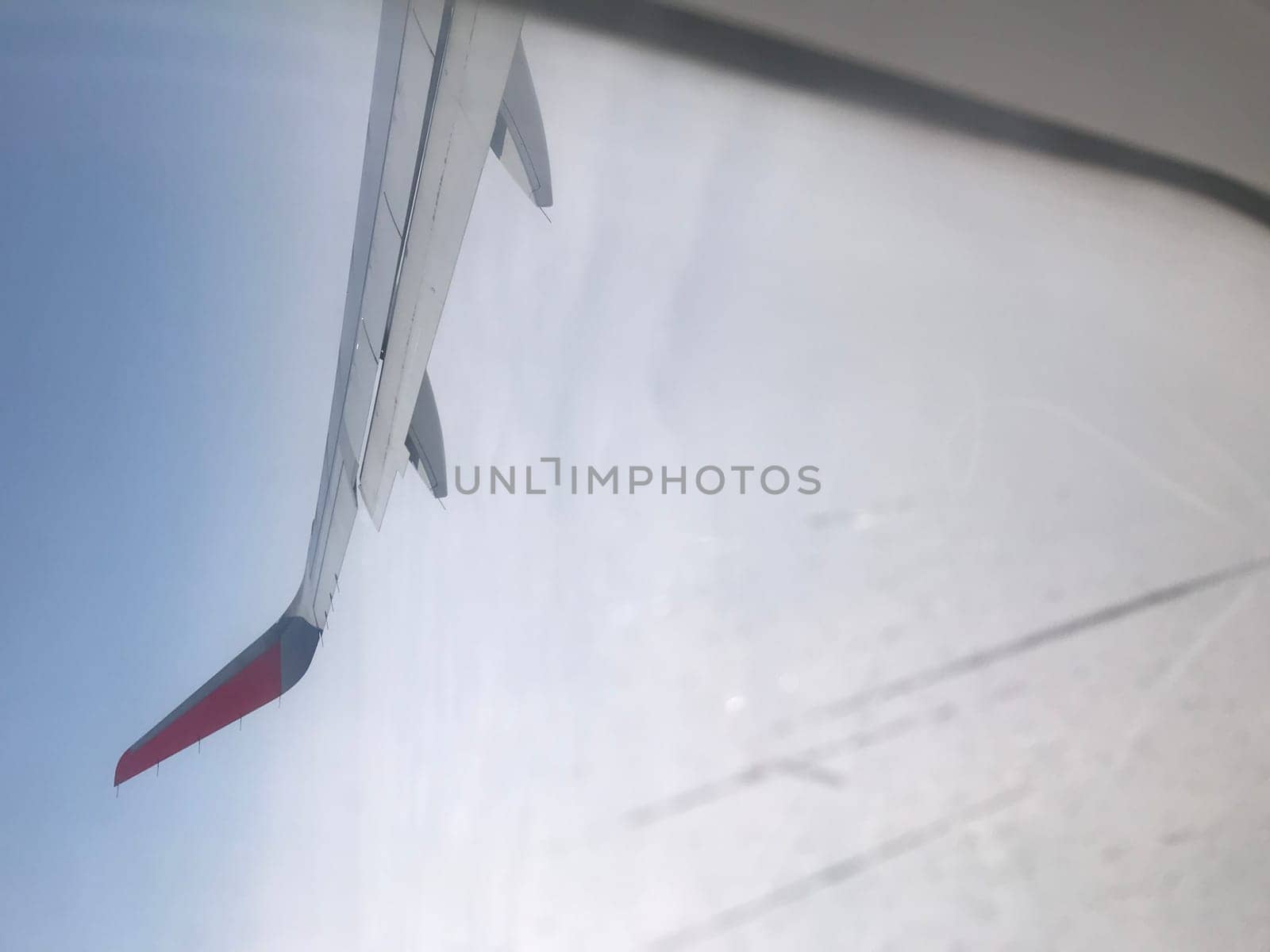 View of an airplane wing through the cabin window against a bright sky background