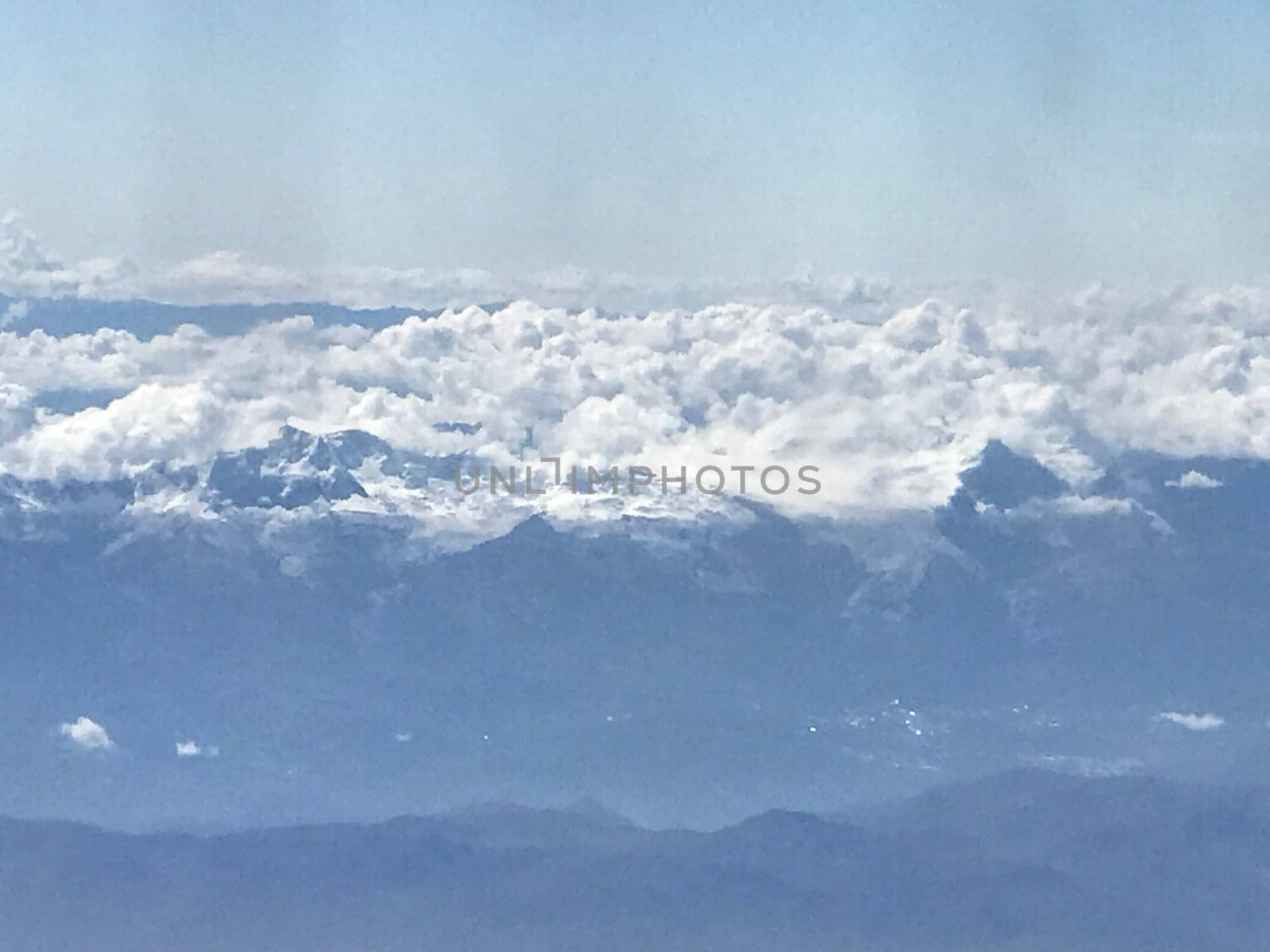 Aerial view showing the top of snow-capped mountains emerging from fluffy clouds