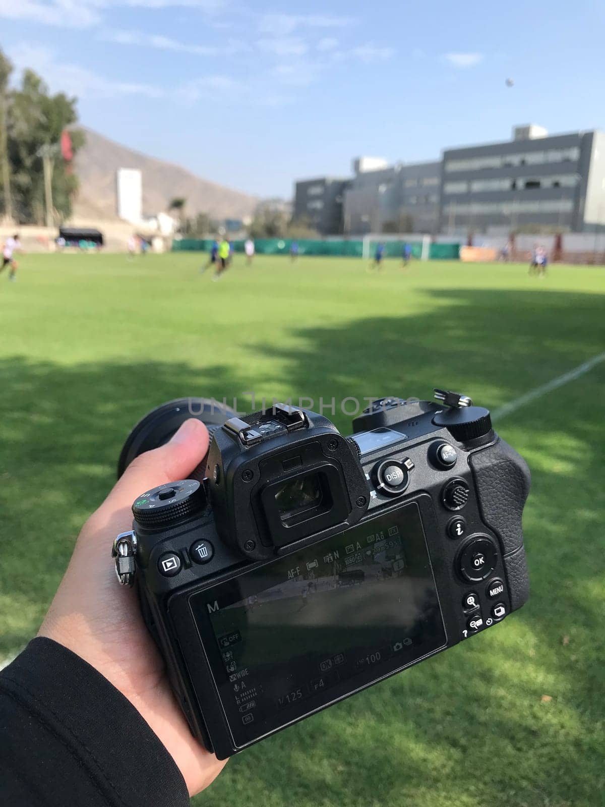 Close-up of a dslr camera in hand with a soccer match in the background