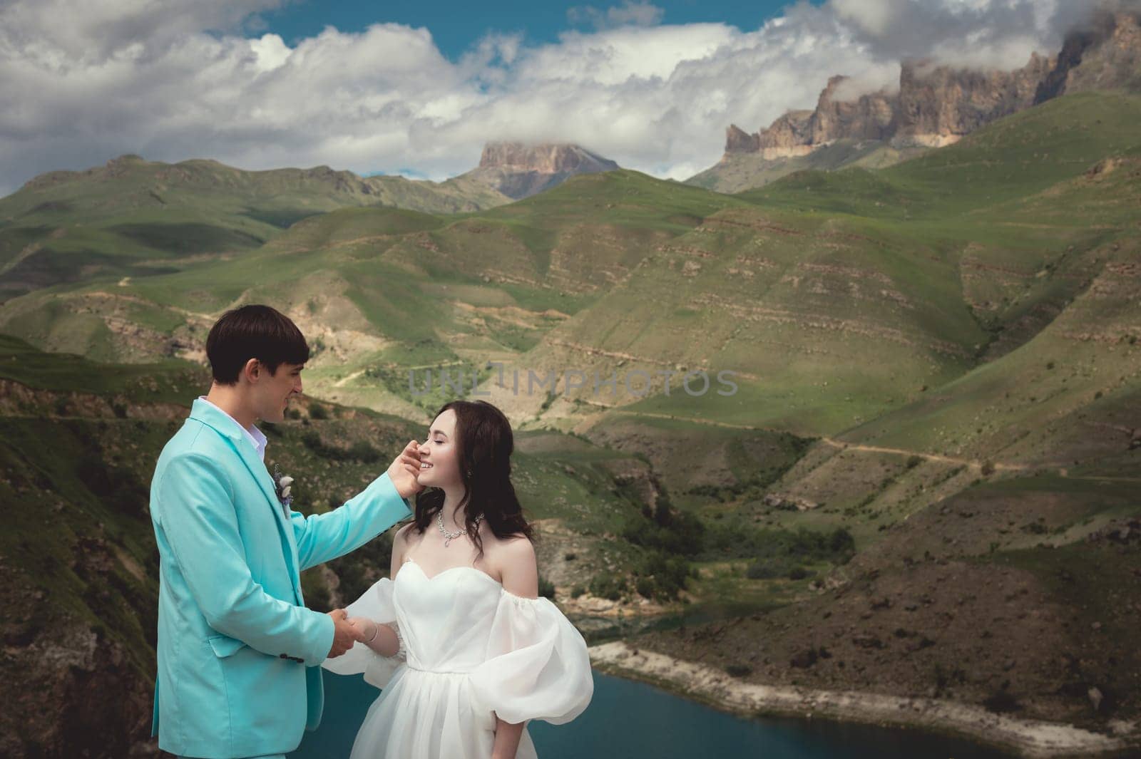 A young man and his wife stand in an embrace high in the mountains against the backdrop of epic rocks on a sunny day. Newlyweds wedding couple in the mountains.