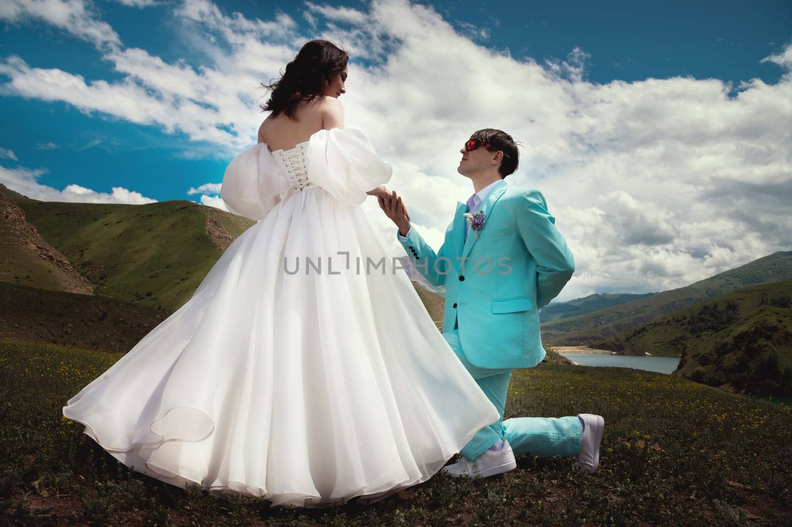 A beautiful wedding couple hugs tenderly against the backdrop of a mountain river and lake, the bride's long white dress.