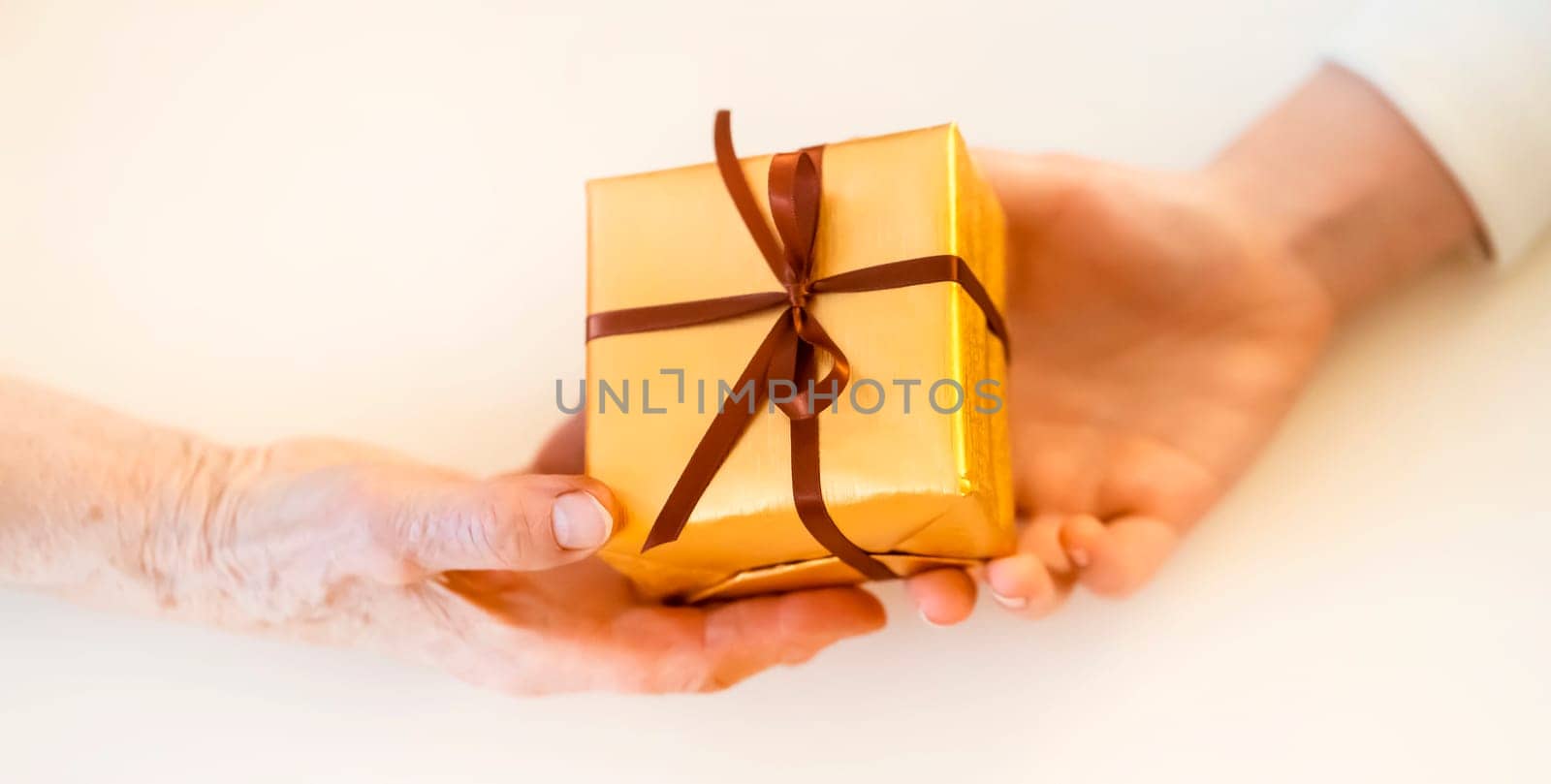 Female hands hold a gift closeup, top view. A young girl gives a nice packed surprise to her mother, grandmother with love, remembers elderly relatives, visits during holidays, takes care of them.