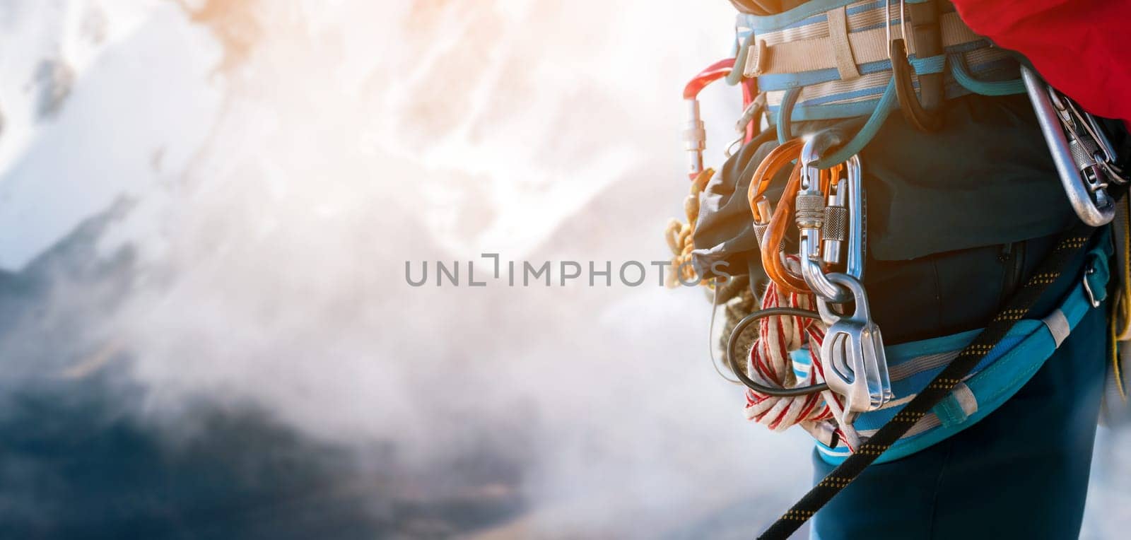 Young man traveler alpinist climbs to the top of a snowy mountain with climbing equipment, harness, carabiners, rope, a beautiful view on the background.