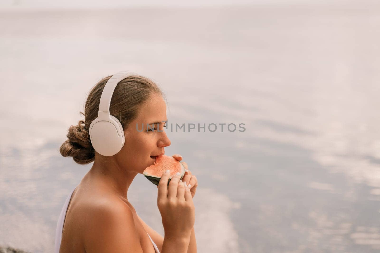 A woman is eating a watermelon while wearing headphones. The scene is peaceful and relaxing, with the woman enjoying her snack in a serene environment