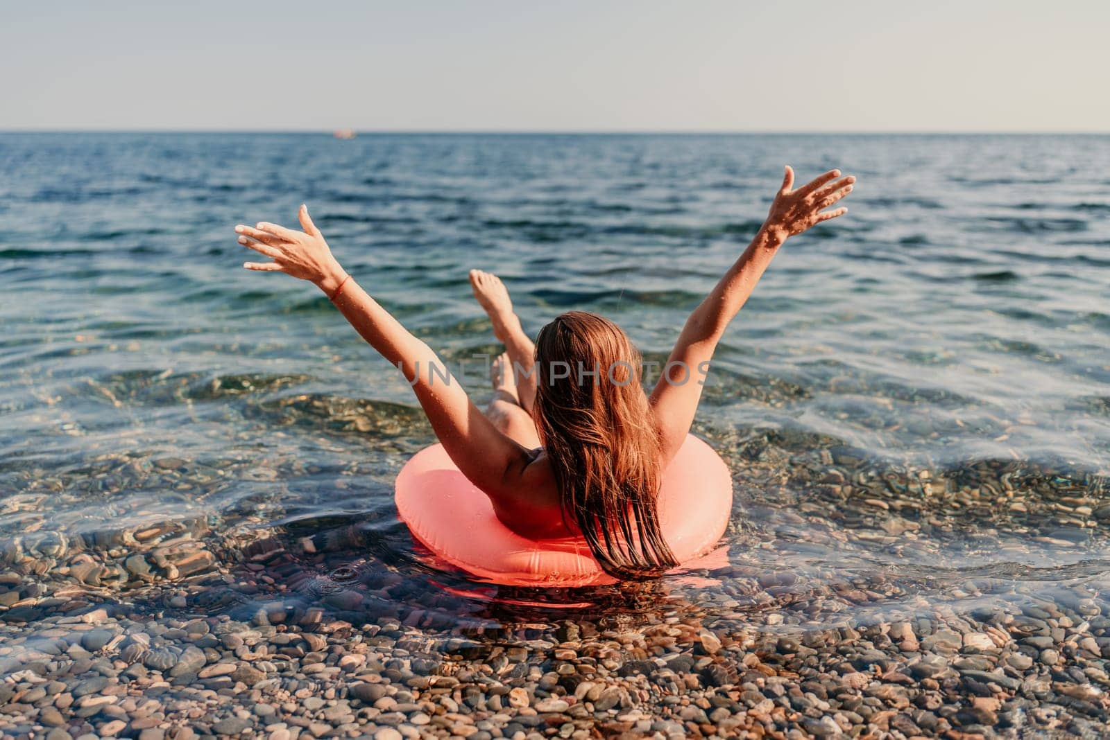 A woman is in the ocean on a red inflatable raft. She is smiling and she is enjoying herself