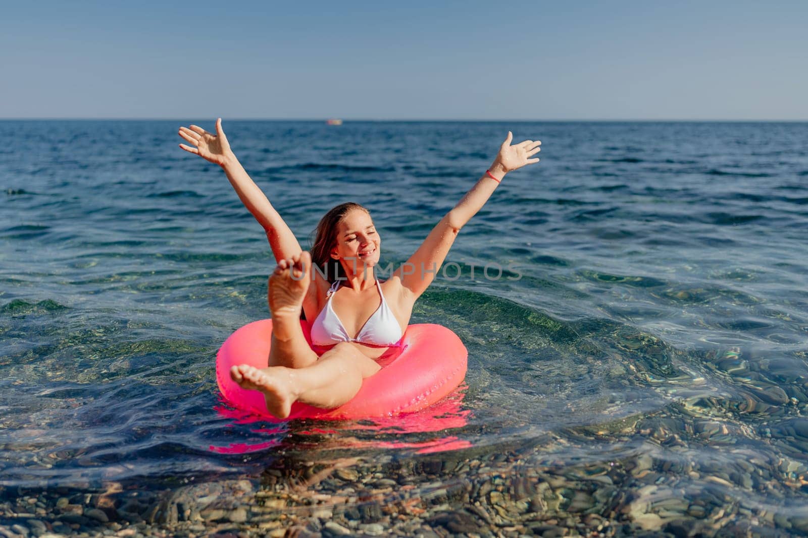 A woman is floating on a pink inflatable raft in the ocean. She is smiling and she is enjoying herself