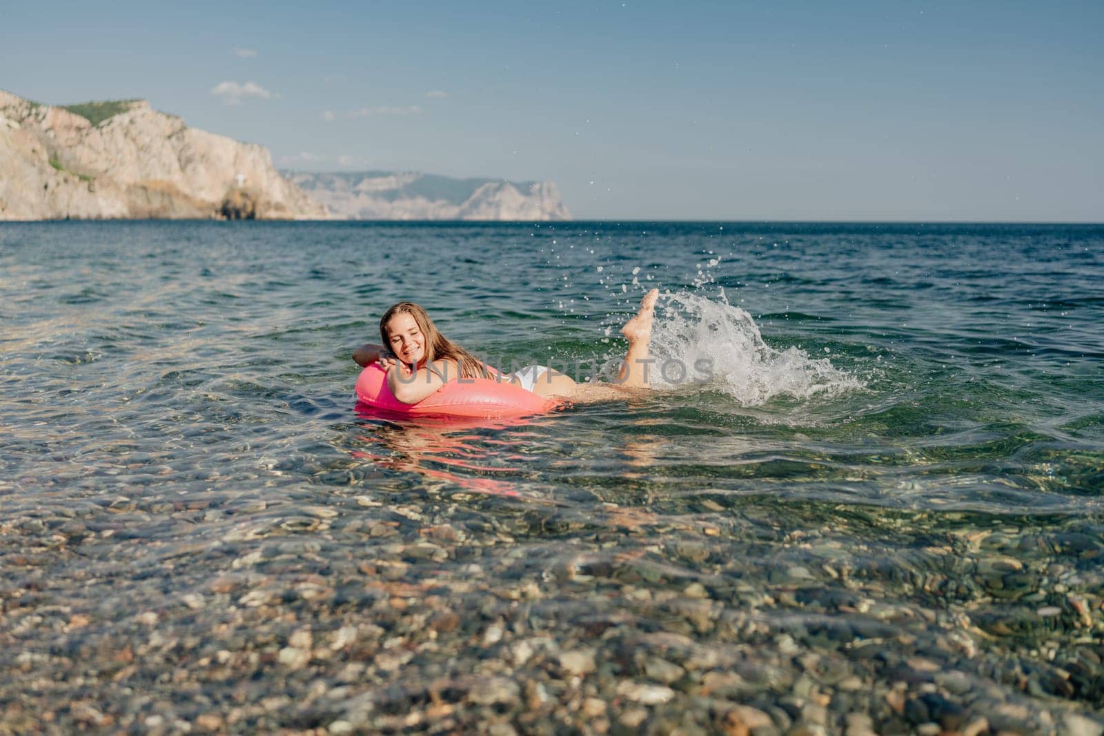 A girl is in the ocean on a pink float. She is smiling and enjoying herself. The water is calm and clear, and the sky is blue