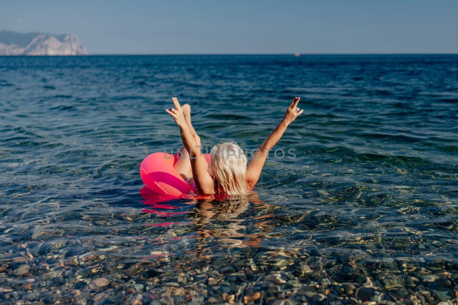 A woman in a red bikini is in the ocean, holding her hands up in the air. She is surrounded by rocks and the water is clear