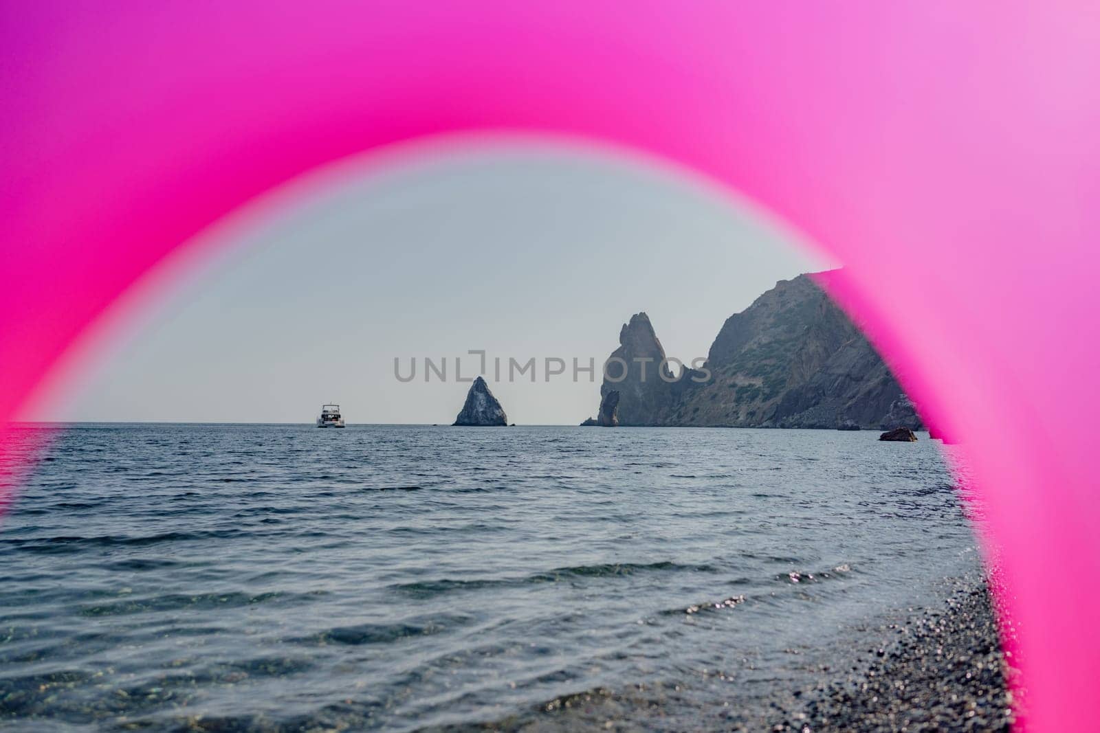 A pinkish purple arch is seen over the ocean. The arch is in the middle of the ocean and is surrounded by water