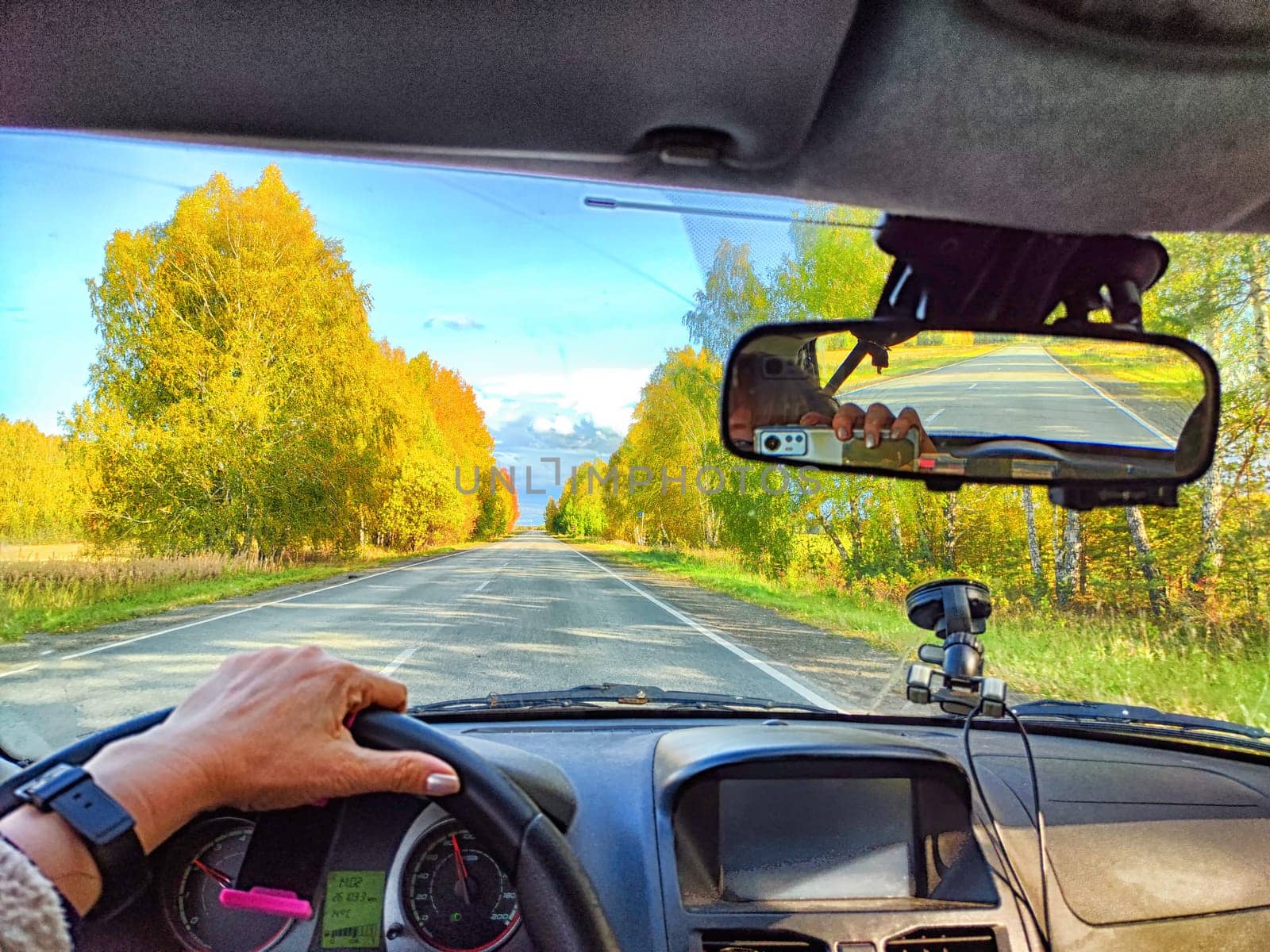 Car salon, windshield, hand on steering wheel and landscape in sunny day. View from driver on nature and Road. Single traveler. Partial focus. Blurred